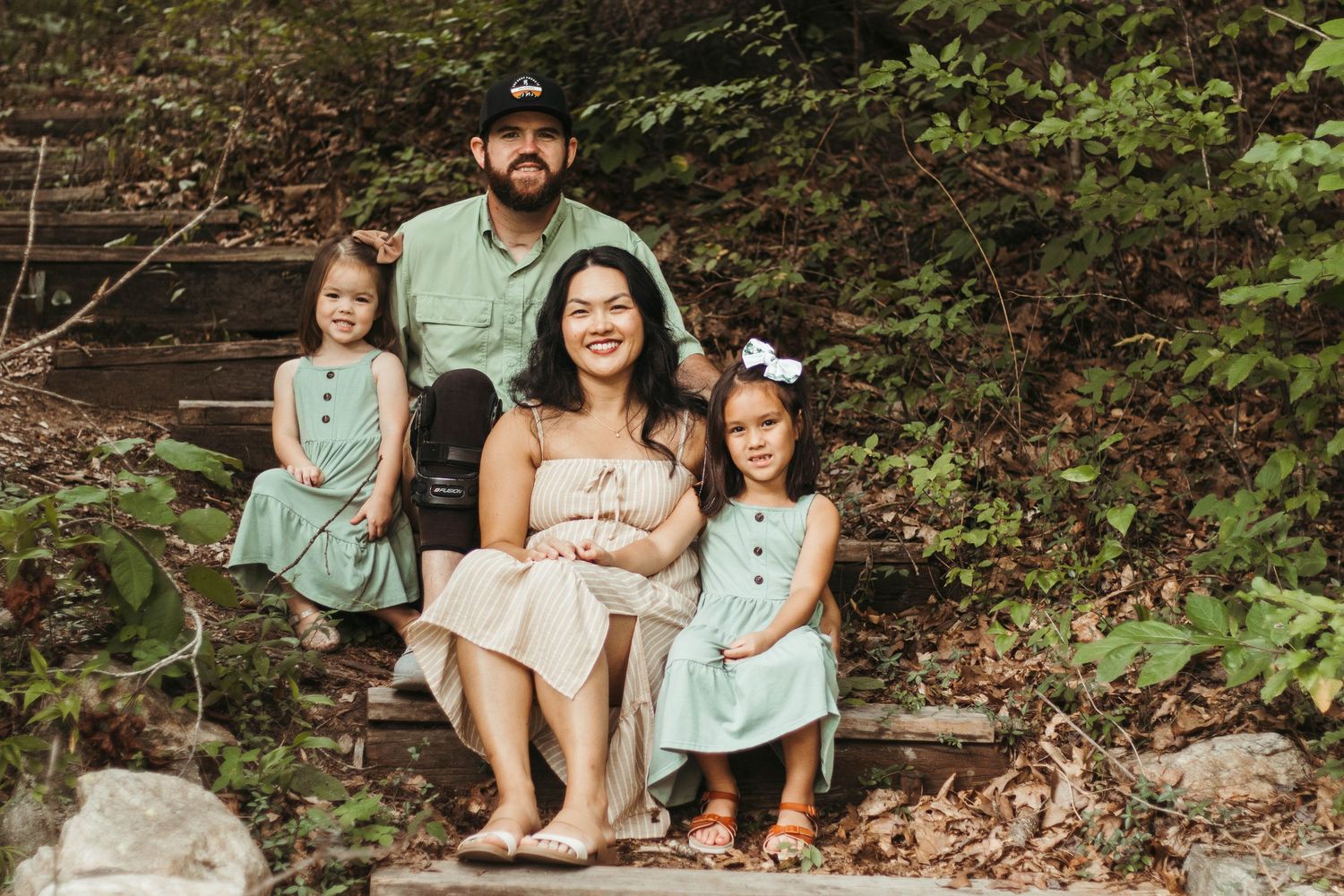 Family sitting together on stone steps in a wooded outdoor setting at Henderson Falls Park wearing coordinated mint green and white outfits.