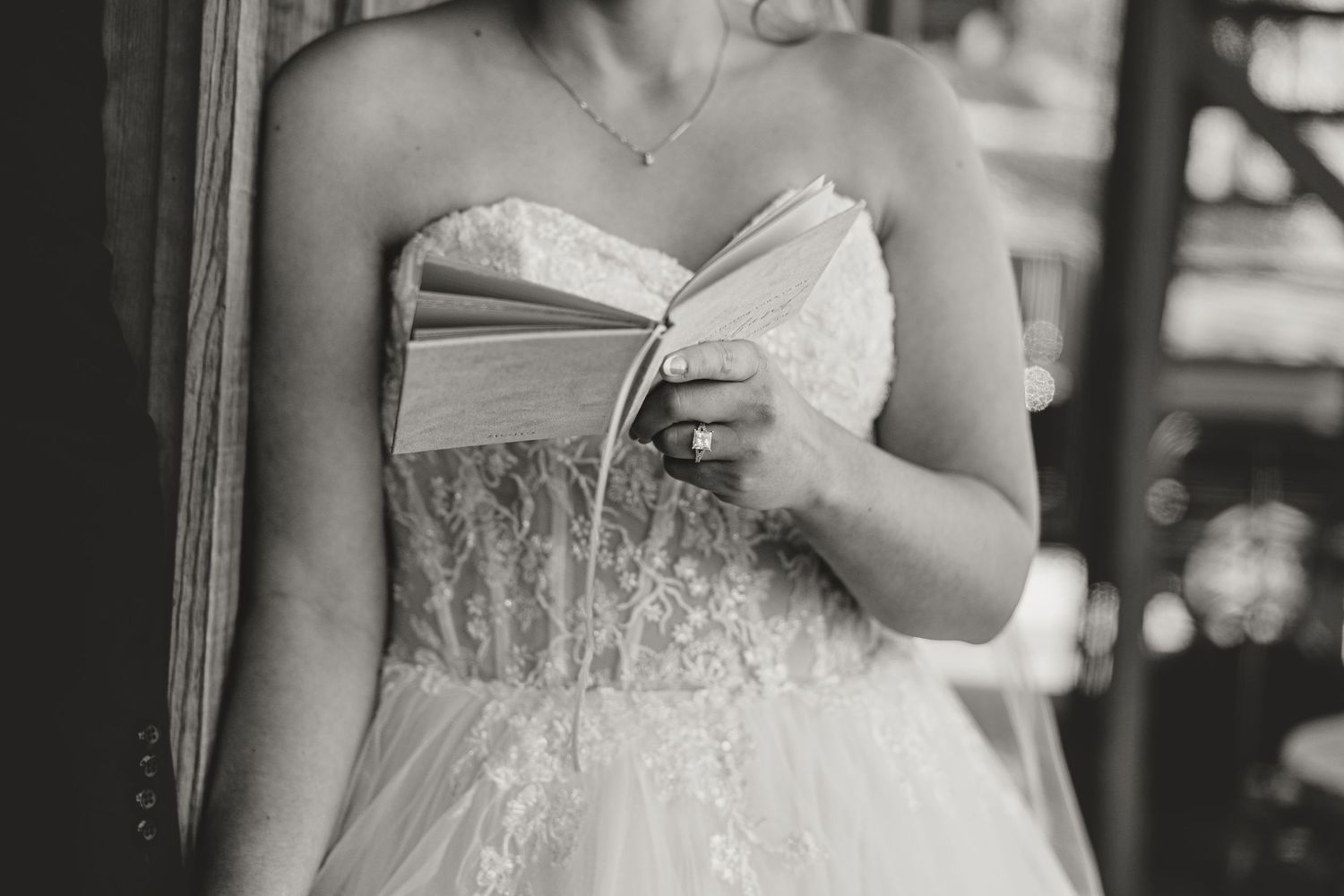 Bride in strapless lace wedding gown holding a book, black and white wedding photo.