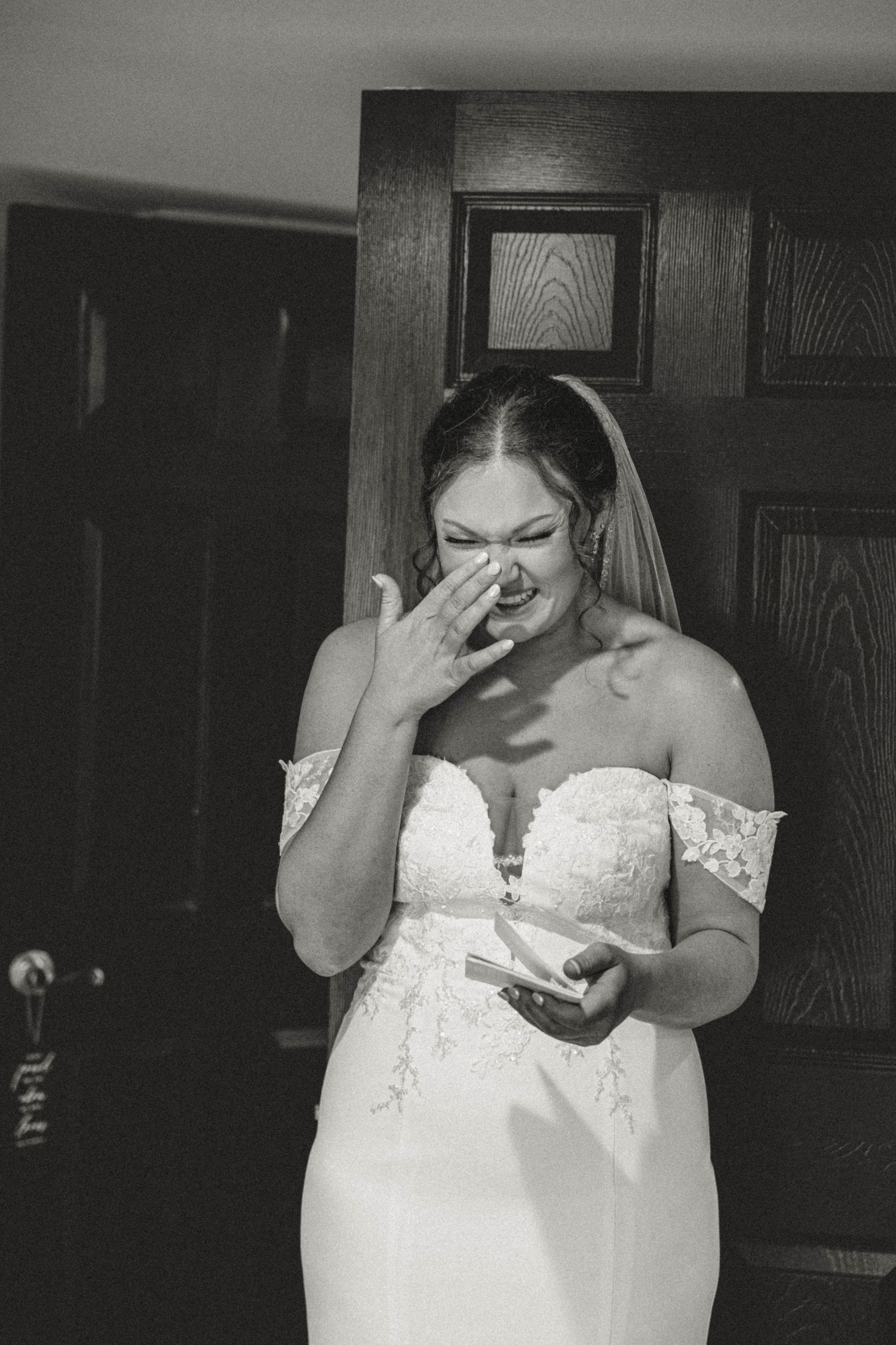A bride in a white lace dress showing emotional reactions during a special wedding moment indoors.