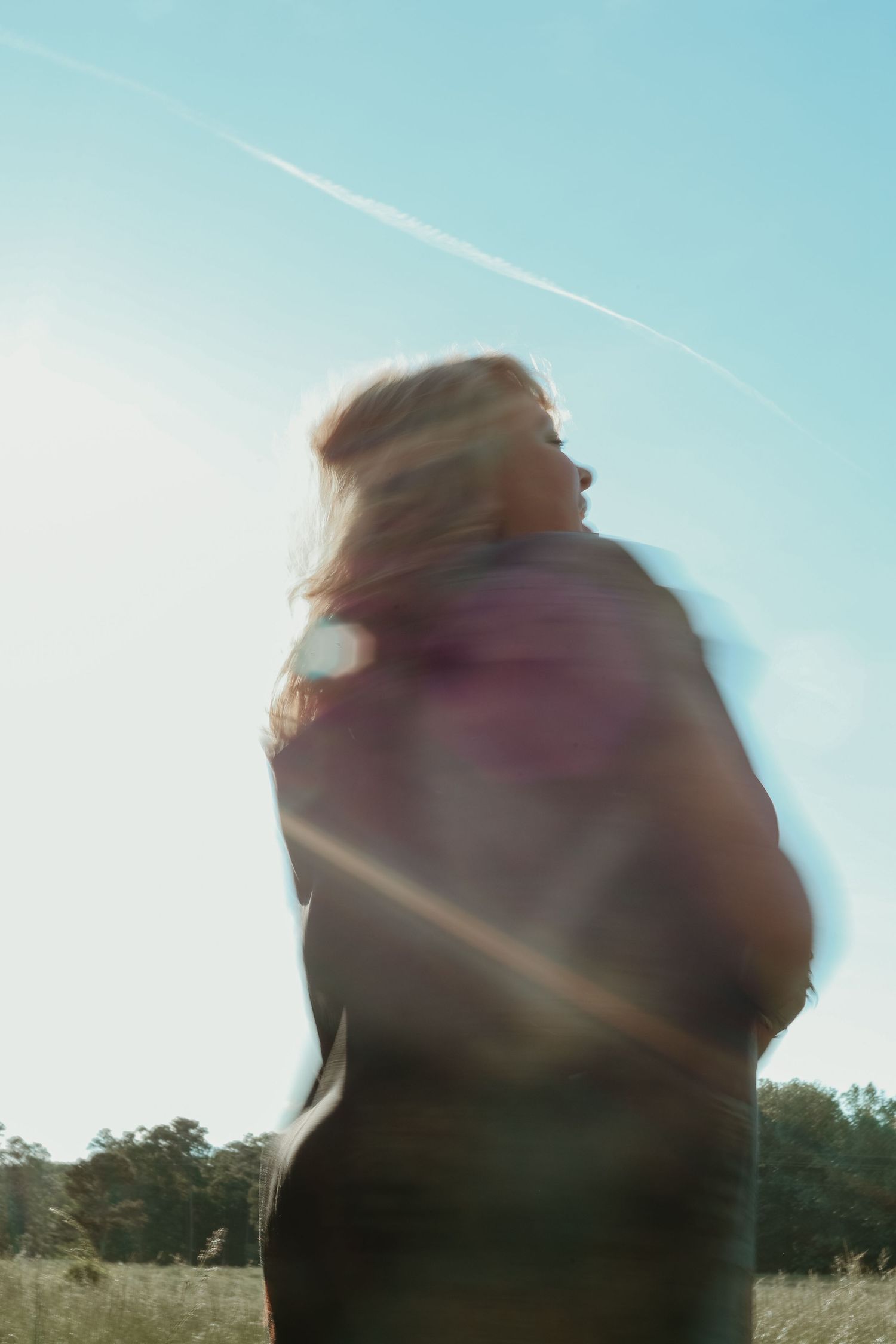 A blurred artistic portrait silhouette against bright blue sky with sun flare and contrail in background located in northeast GA.