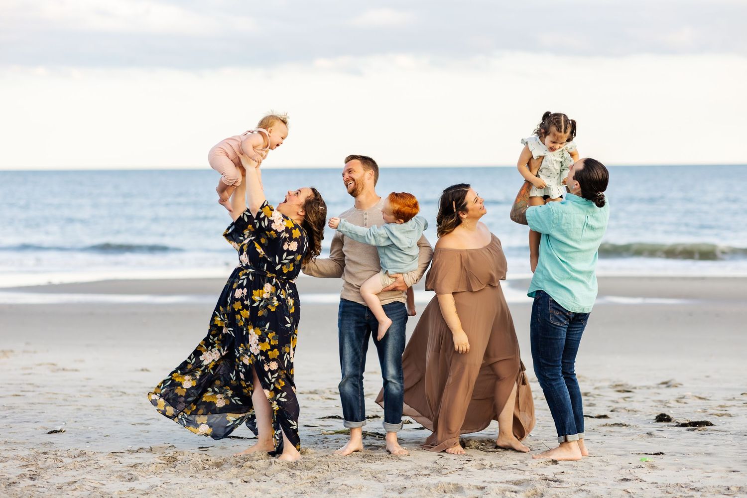 Families playing and lifting children on beach at sunset.