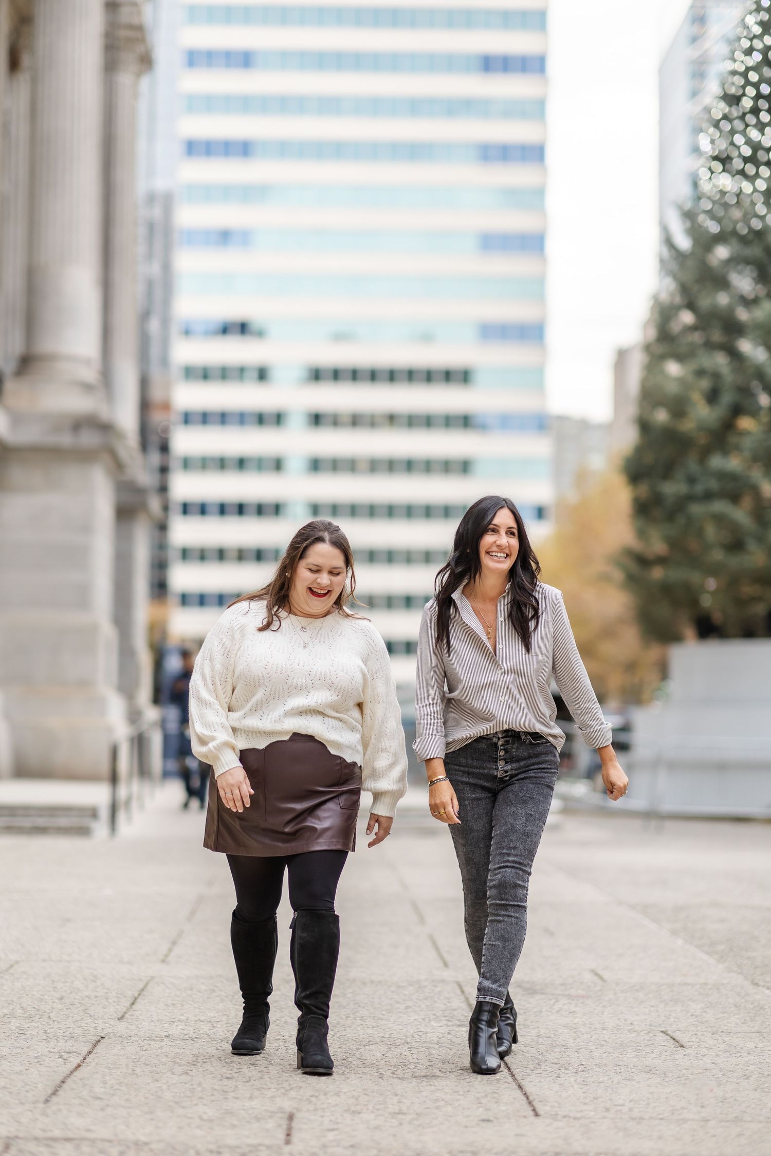 Two people walking and laughing together on a city sidewalk with office buildings visible in the background.