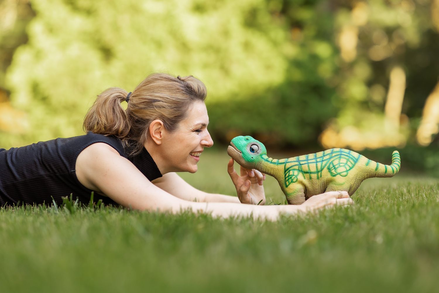 Robot ethicist Kate Darling lies down in the grass to play with small dinosaur robot