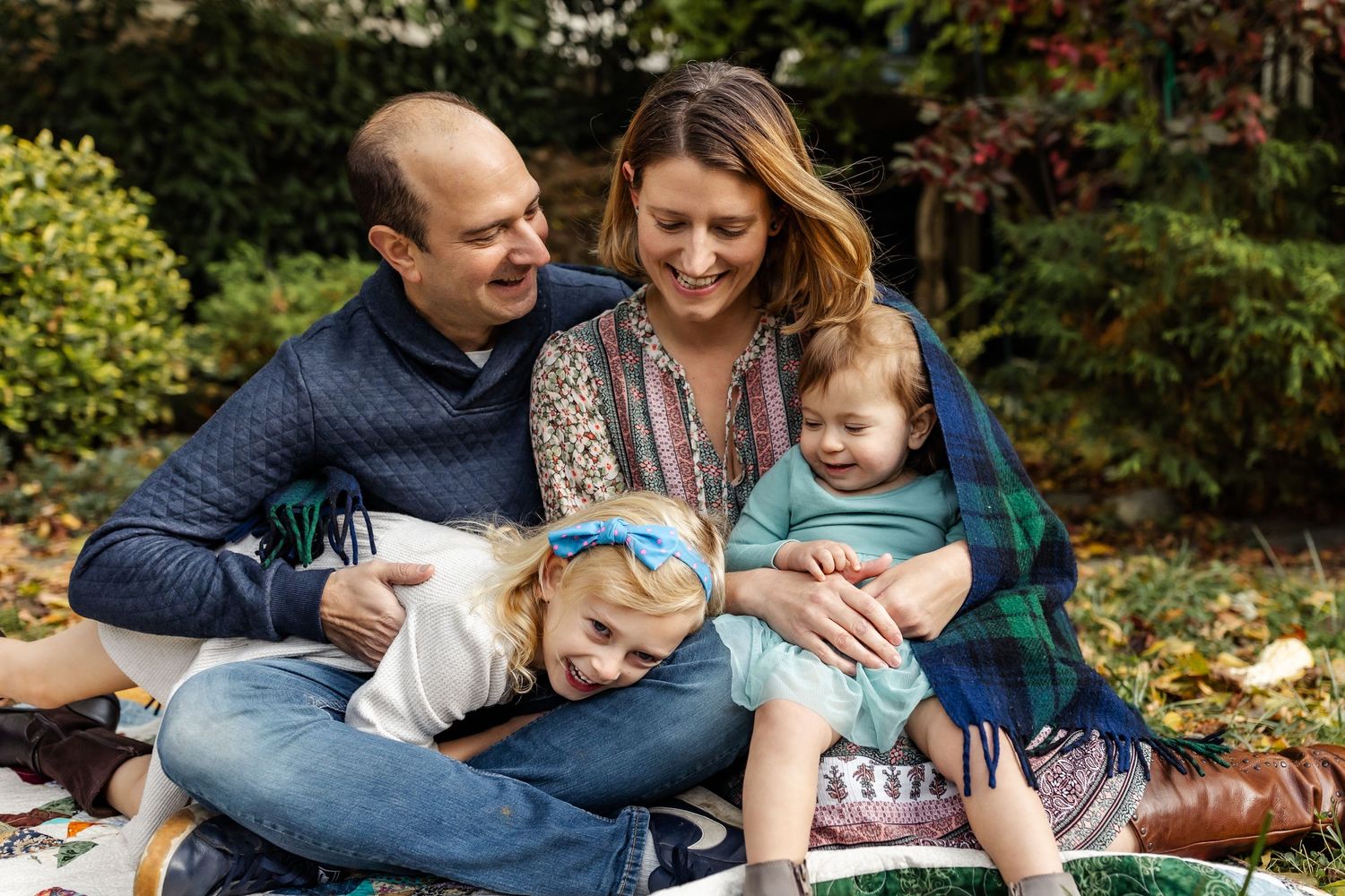 Family sharing a relaxed moment together on a blanket in an autumn garden setting.
