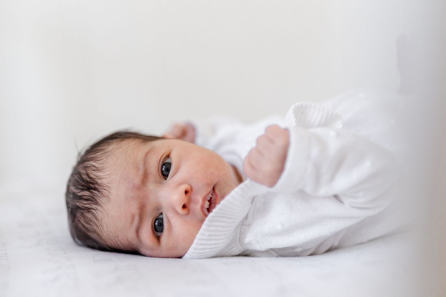 Newborn baby in white clothing lying on light colored bedding.