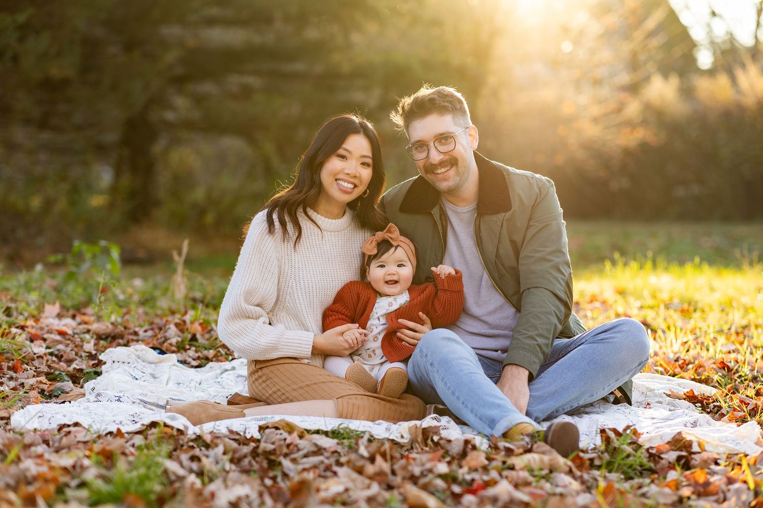 Family portrait session at sunset with warm golden light streaming through autumn leaves.