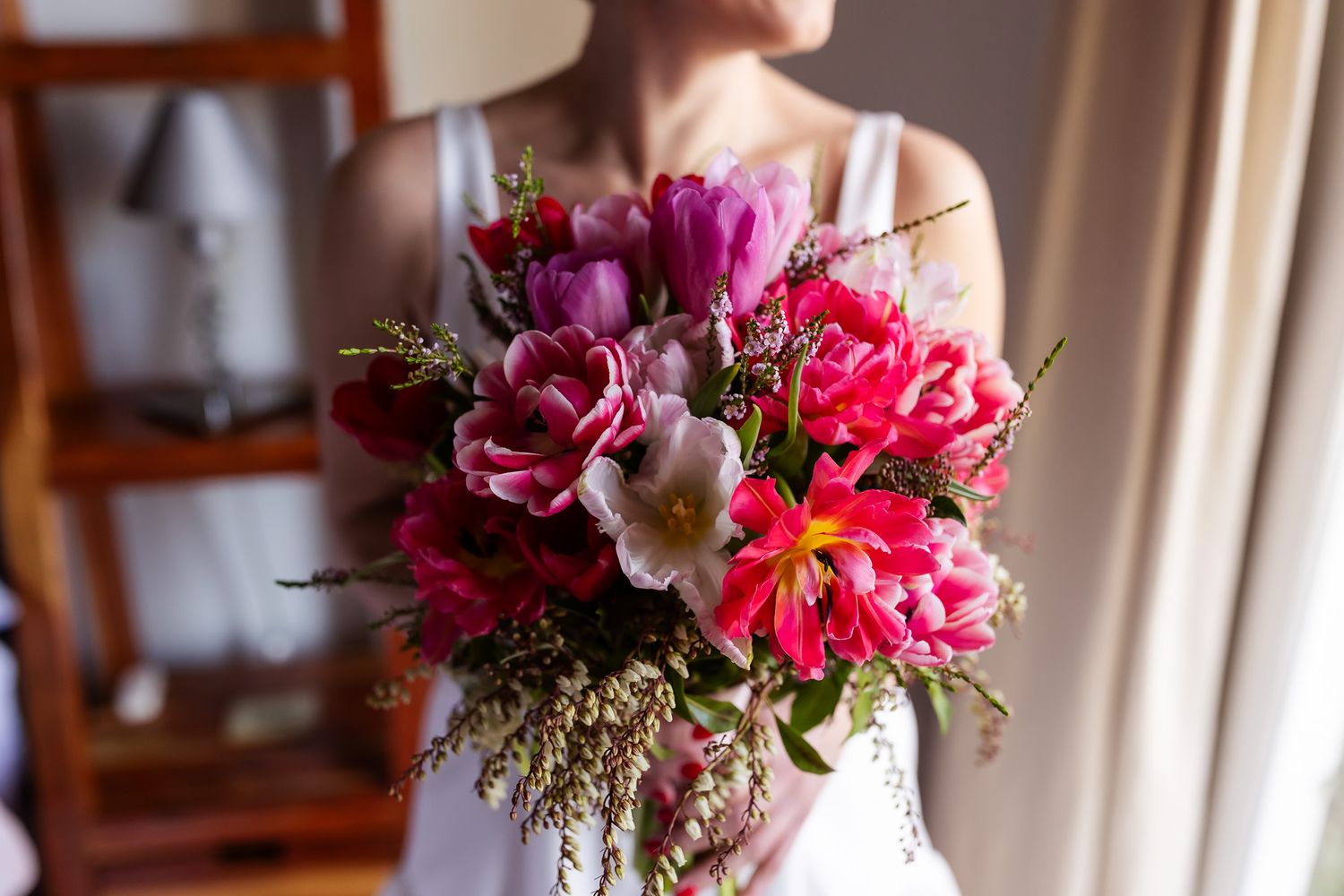 Pink and burgundy floral centerpieces with peonies and greenery decorate tables at an elegant indoor event.