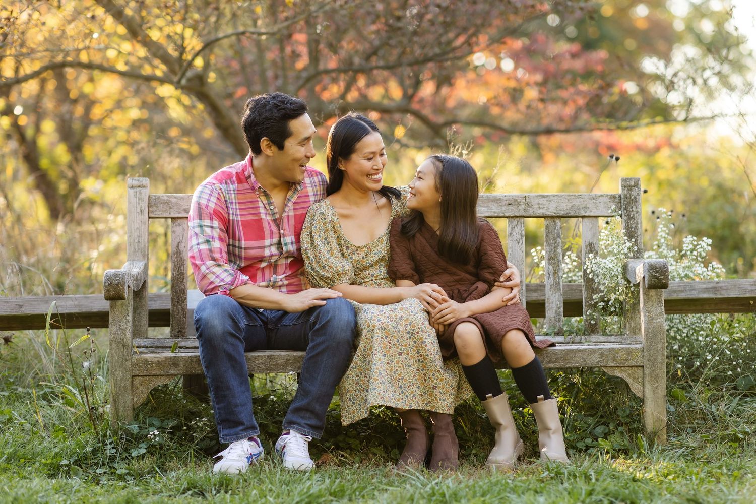 Family shares intimate moment while sitting together on wooden bench in garden.