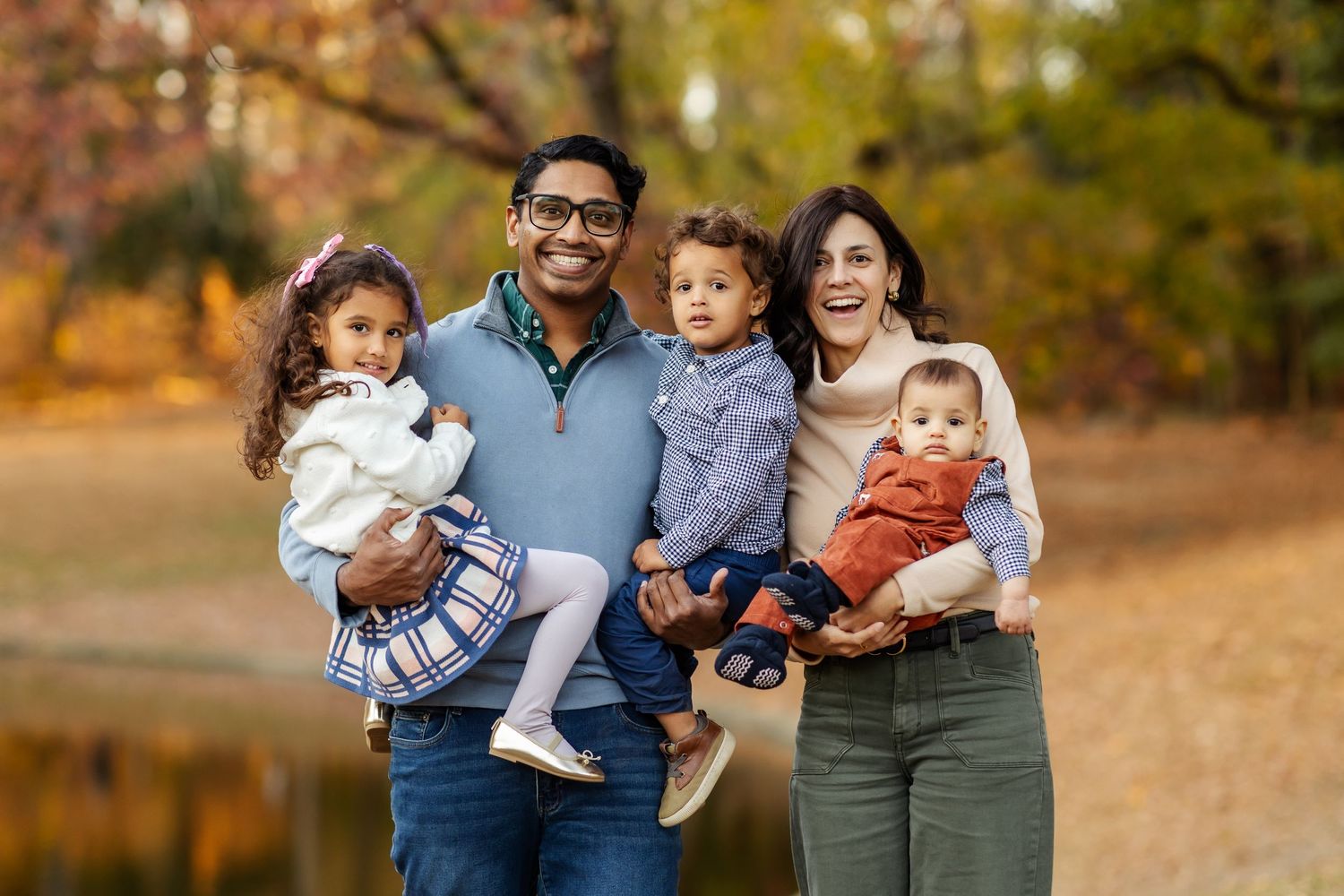 Family poses together for autumn portrait outdoors with a backdrop of fall foliage.