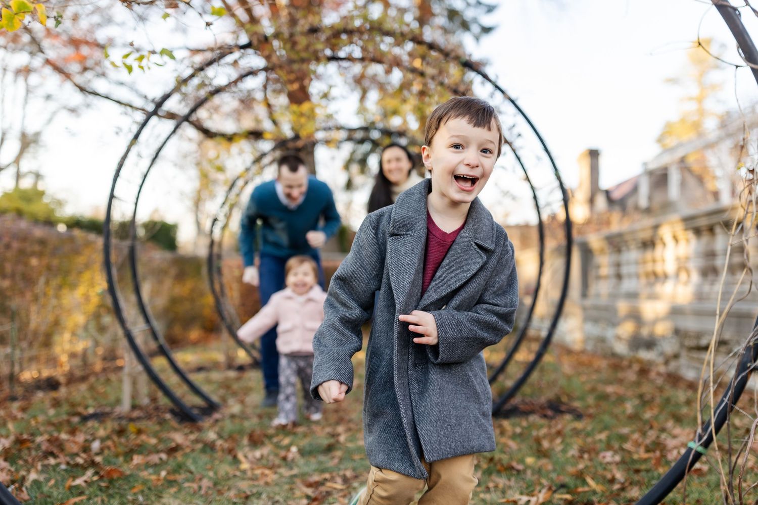 Children playing near a metal garden arch with fallen autumn leaves on the ground.