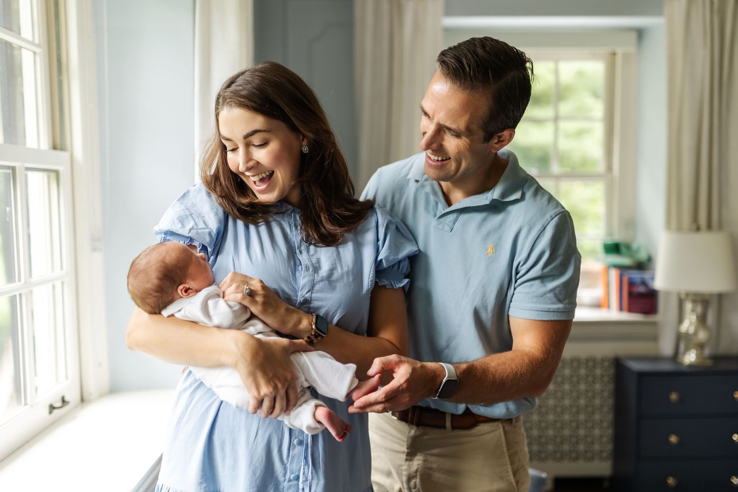 Parents share tender moment with newborn baby by bright window.