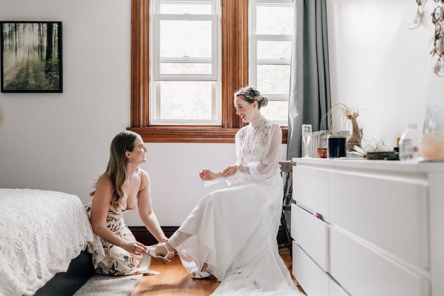 A bride in a white wedding dress sits at a desk in a bright room while getting ready for her special day.