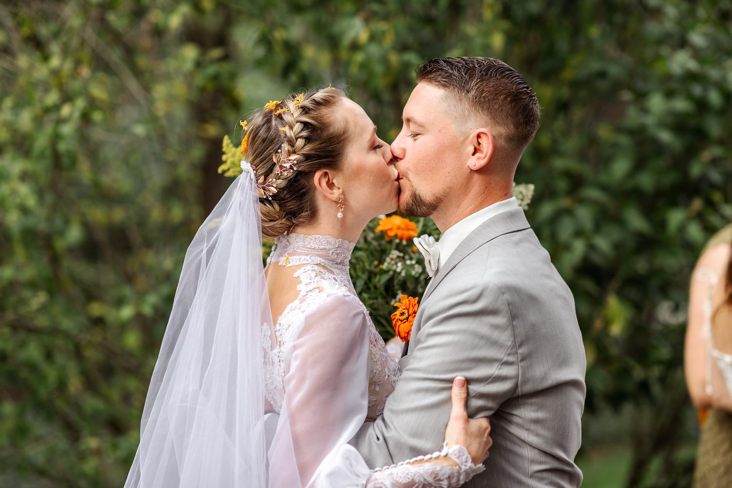 A bride and groom share a romantic kiss in a garden setting with sunflowers and greenery in the background.