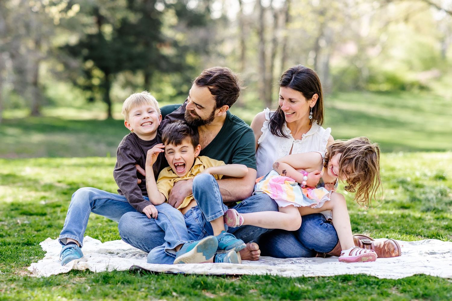 Family relaxing together on a picnic blanket in a sunny spring park.