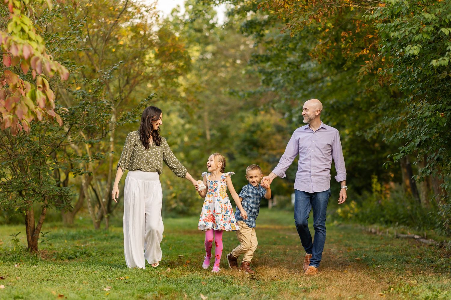 Family of four walking hand-in-hand on a garden path surrounded by colorful autumn trees.
