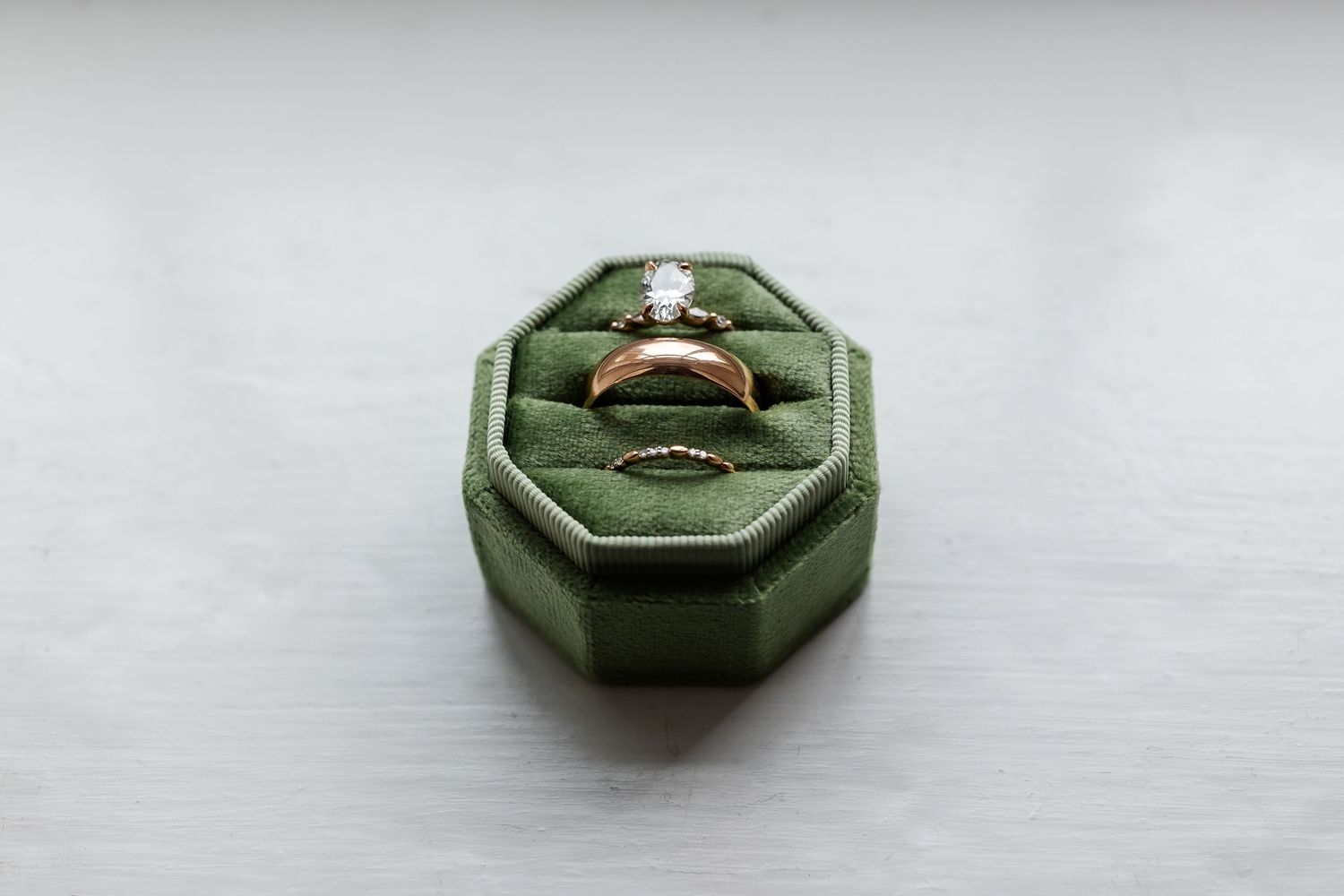 A diamond engagement ring sits in a green velvet octagonal ring box on a light gray surface.