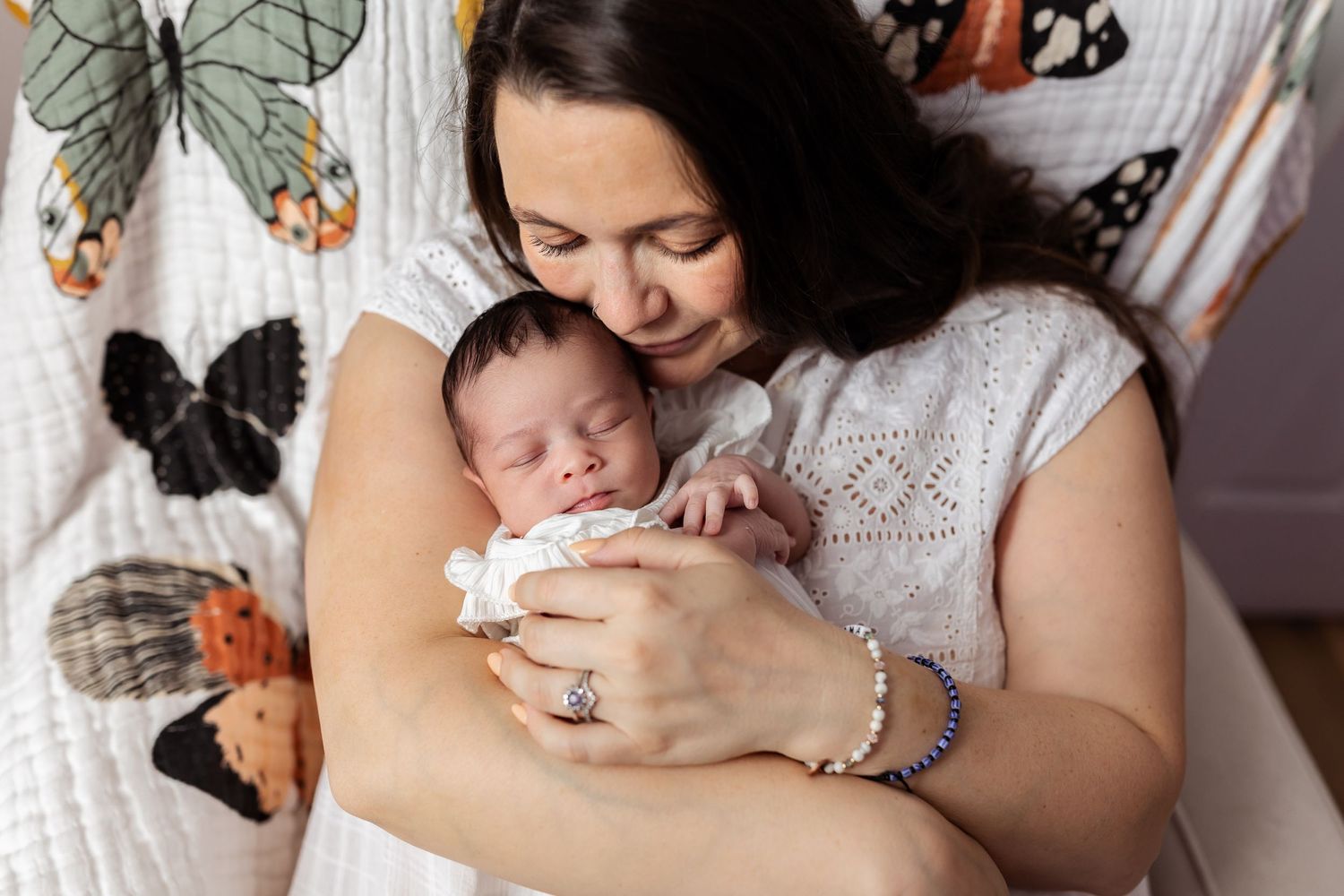 A tender bonding moment with a newborn baby against a butterfly patterned backdrop.