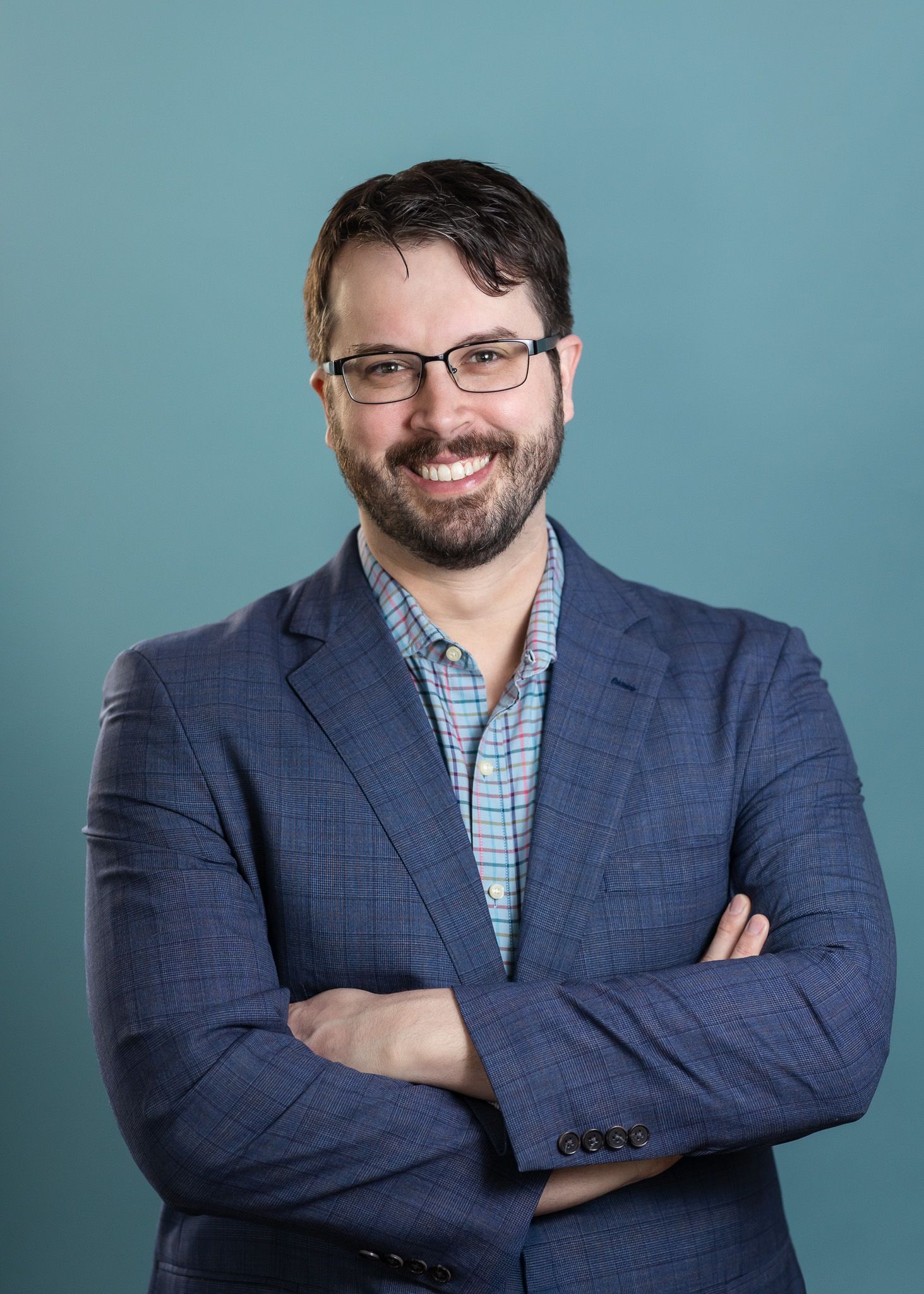Professional headshots of person in navy suit and checkered shirt against blue background.