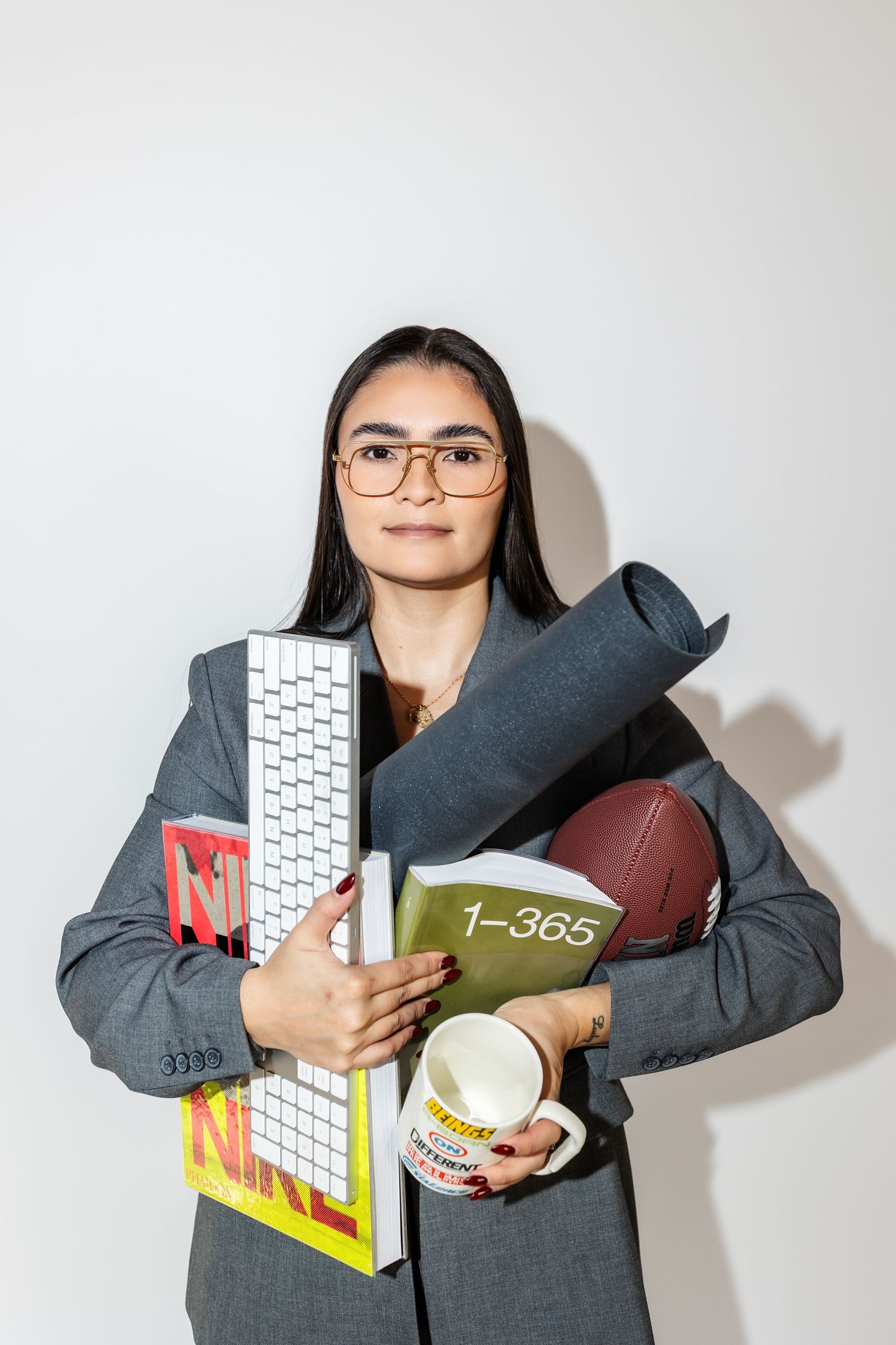 Professional wearing a gray suit holds office supplies and a keyboard while posing against a white background.