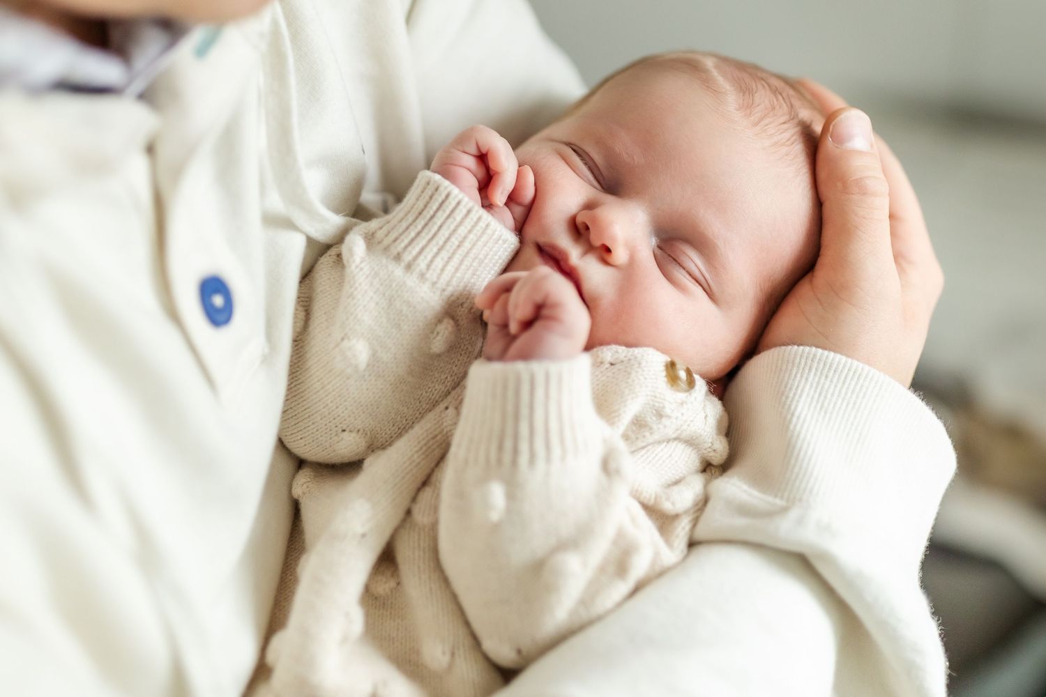 Newborn baby in cream colored knit sweater sleeping peacefully during indoor photoshoot.