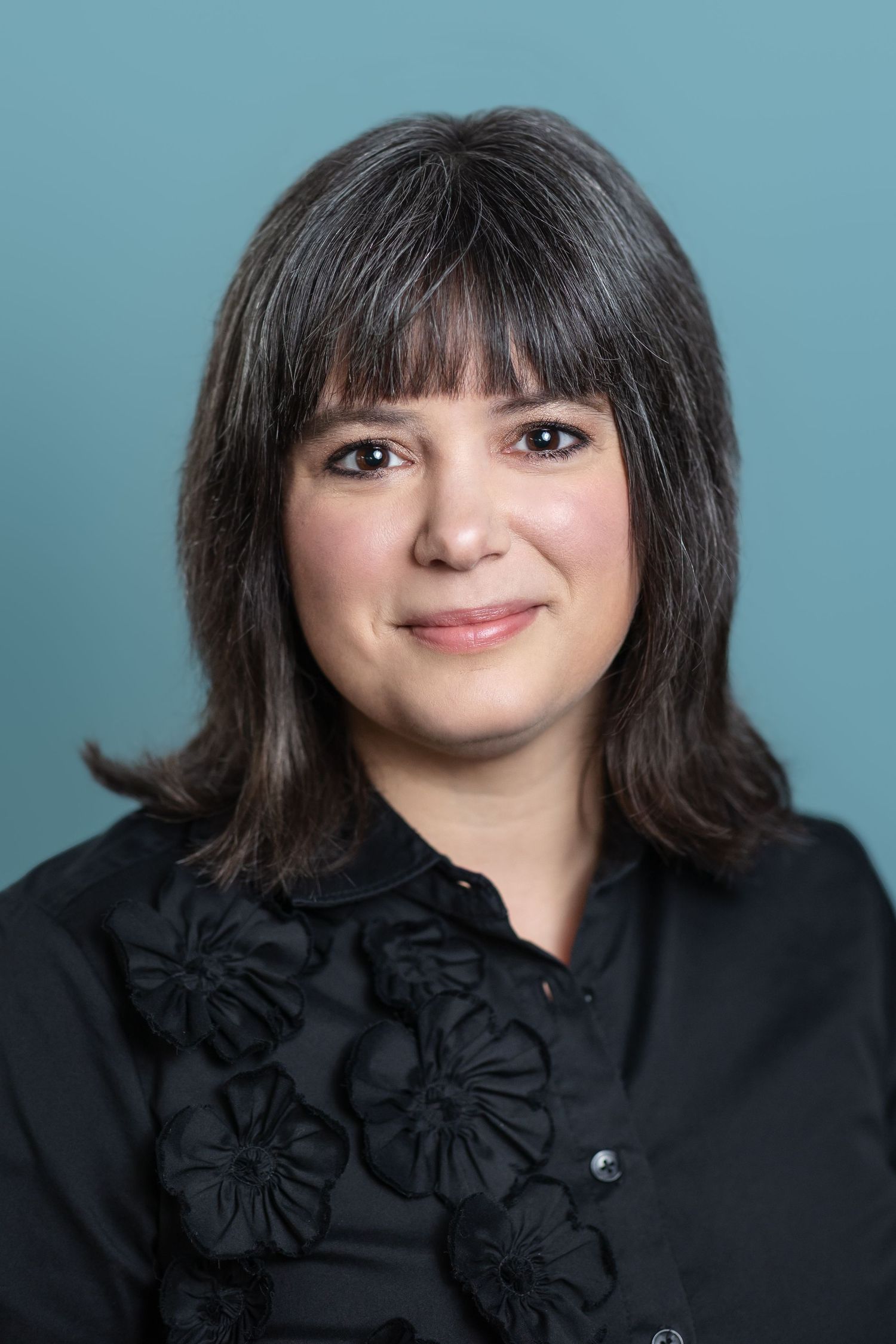 Portrait series against turquoise background wearing black top with flower details.