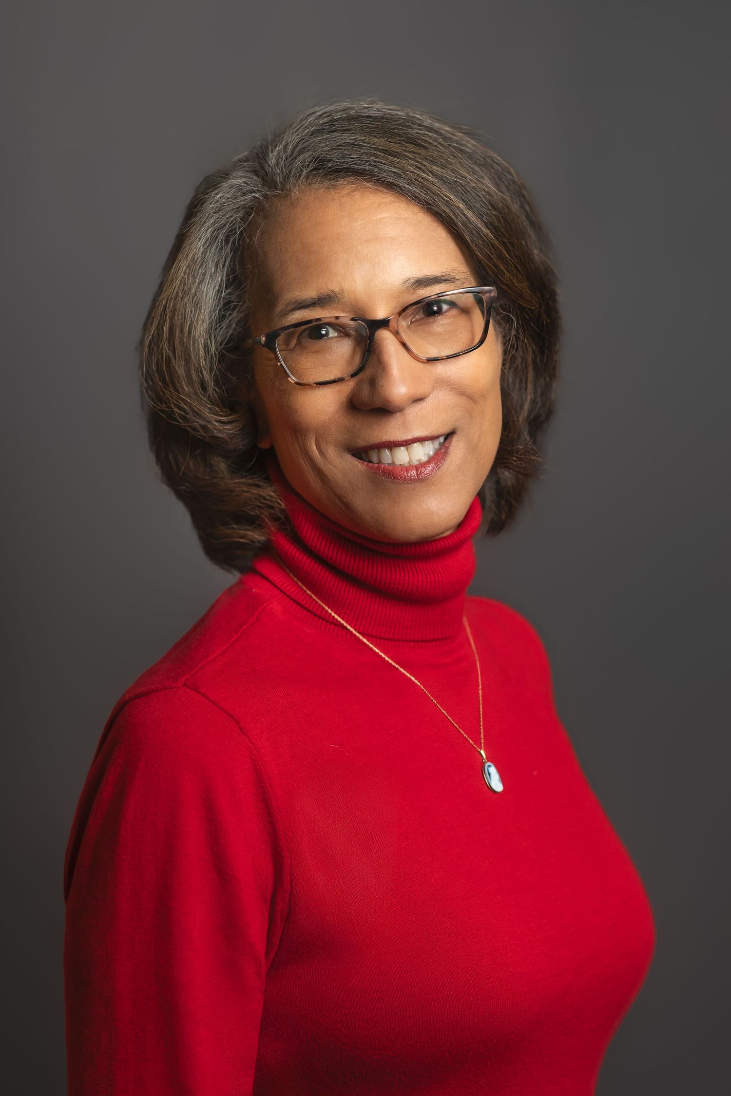 Stylish portrait in red turtleneck sweater and glasses against dark background.