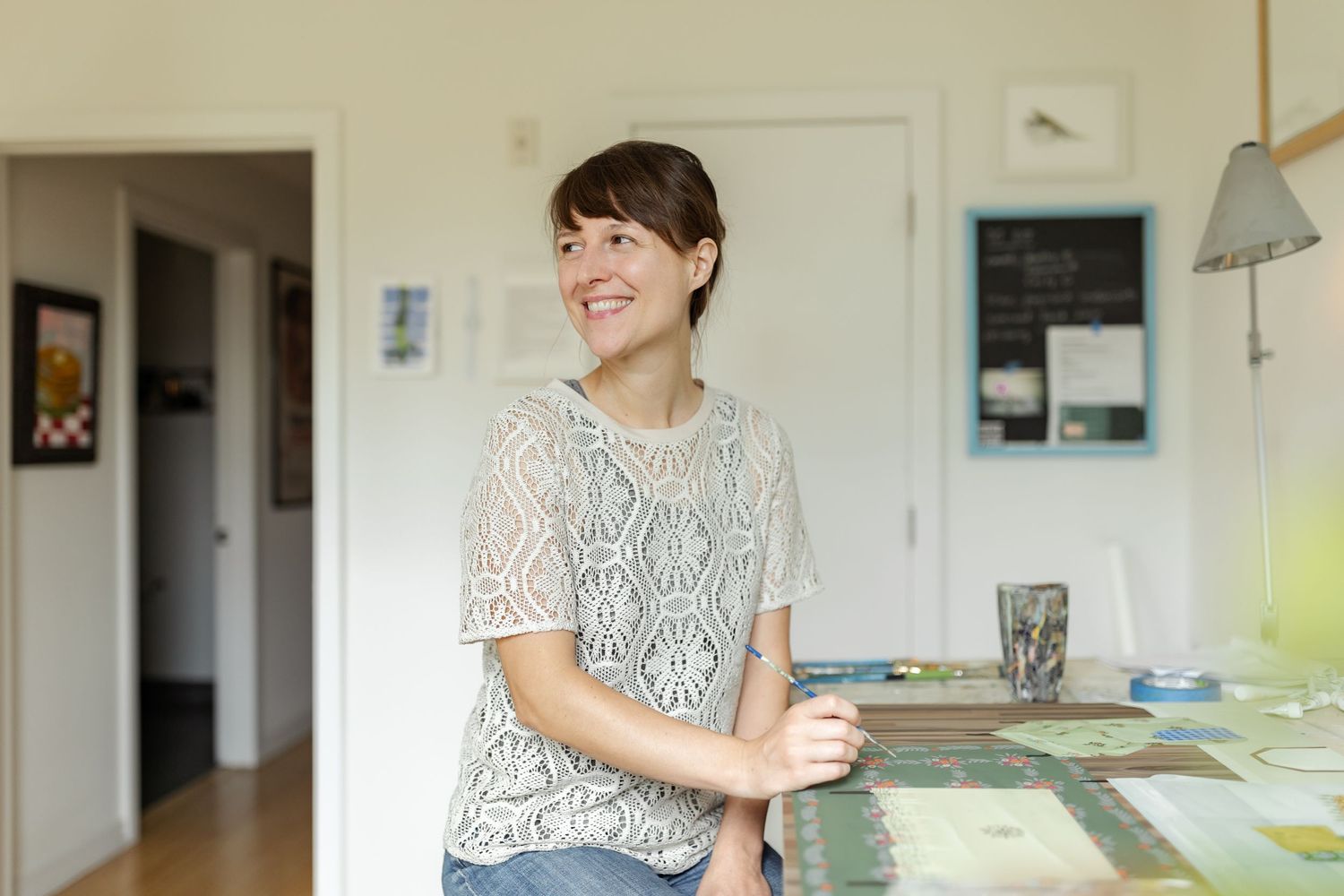 A casual portrait in a bright interior space showing someone wearing a white lace top smiling warmly.