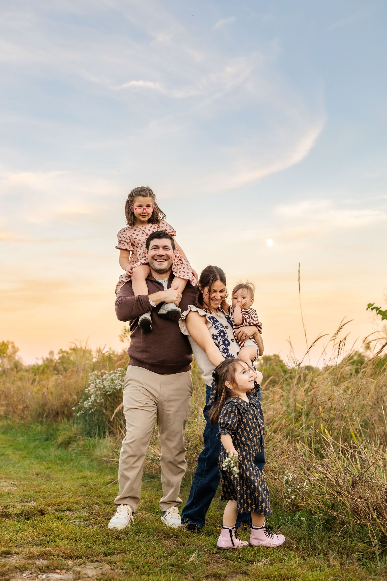 A group plays together on a grassy hillside at sunset, sharing laughter and joy in a candid outdoor photoshoot.