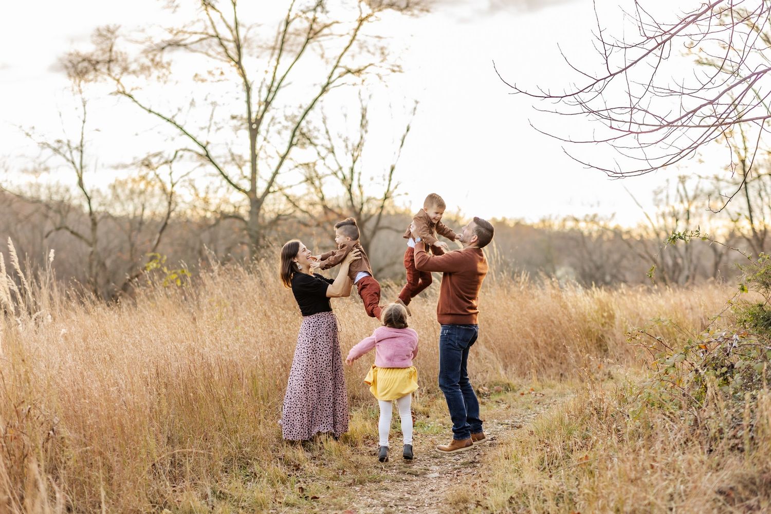 Family enjoying a playful moment together in a tall grass field during golden hour.