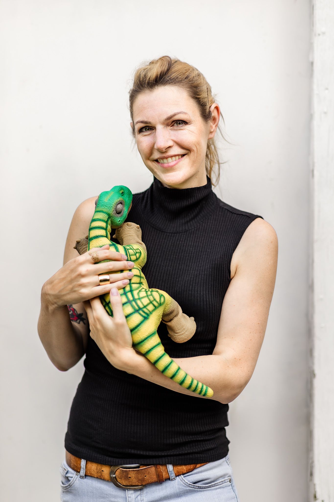 Woman in black shirt stands against a white wall and holds her pleo robot