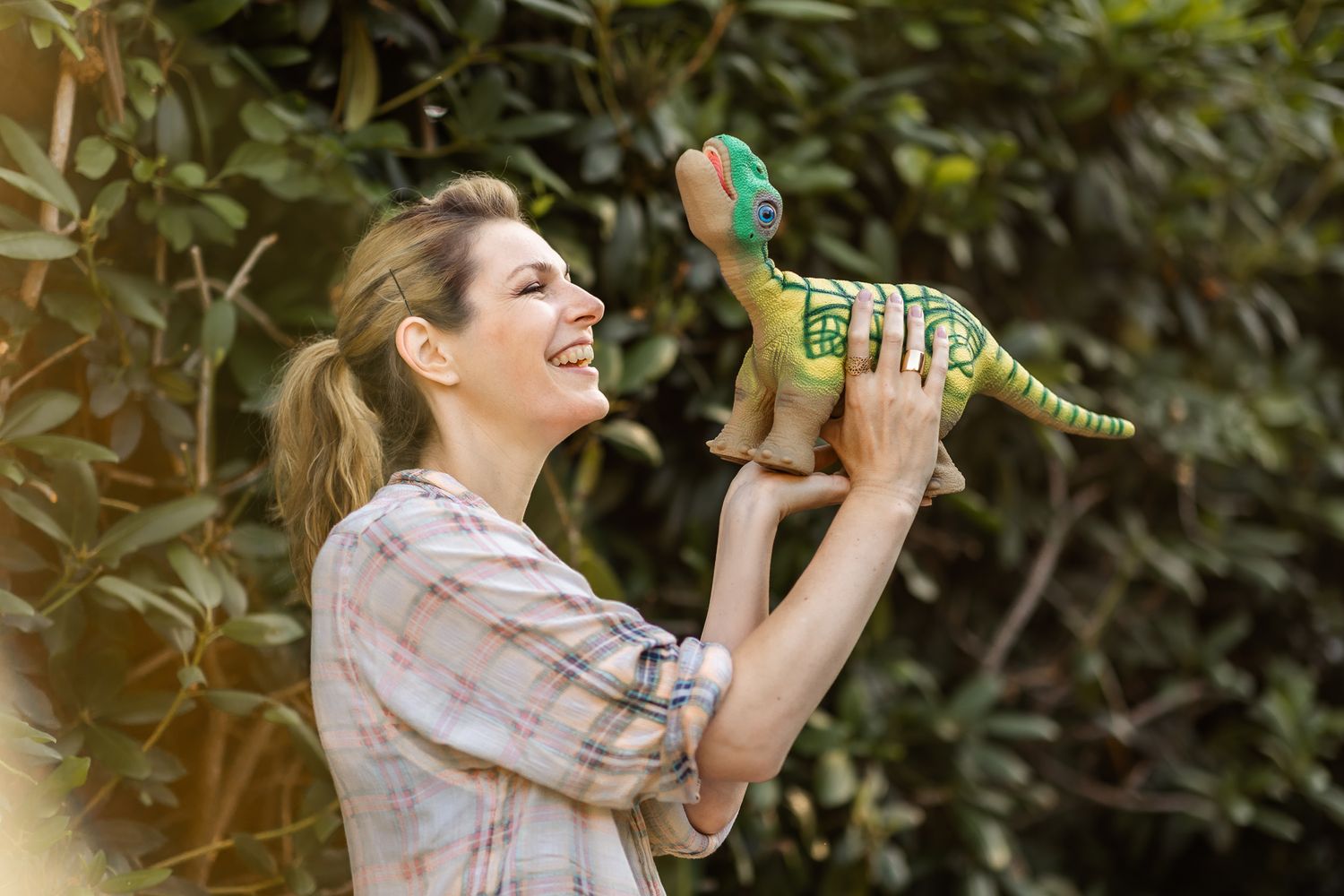 Woman in plaid shirt holds up small dinosaur robot and smiles at it