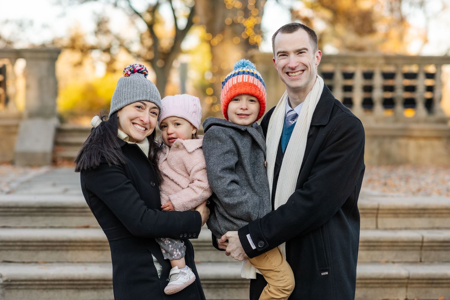 Family in winter attire posing together on outdoor stone steps during autumn.