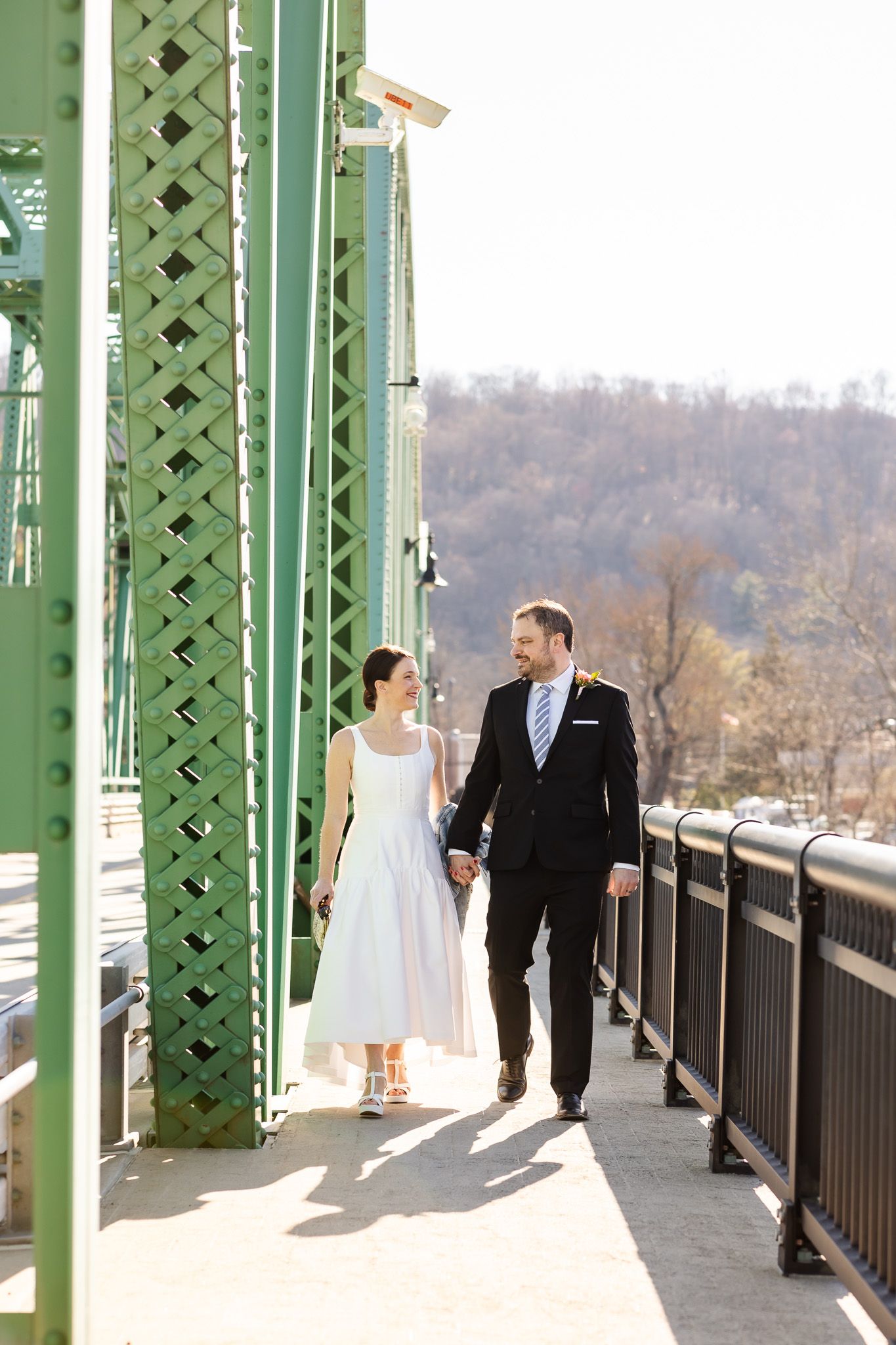 Wedding couple shares romantic moments on a green metal bridge with architectural details and scenic views.