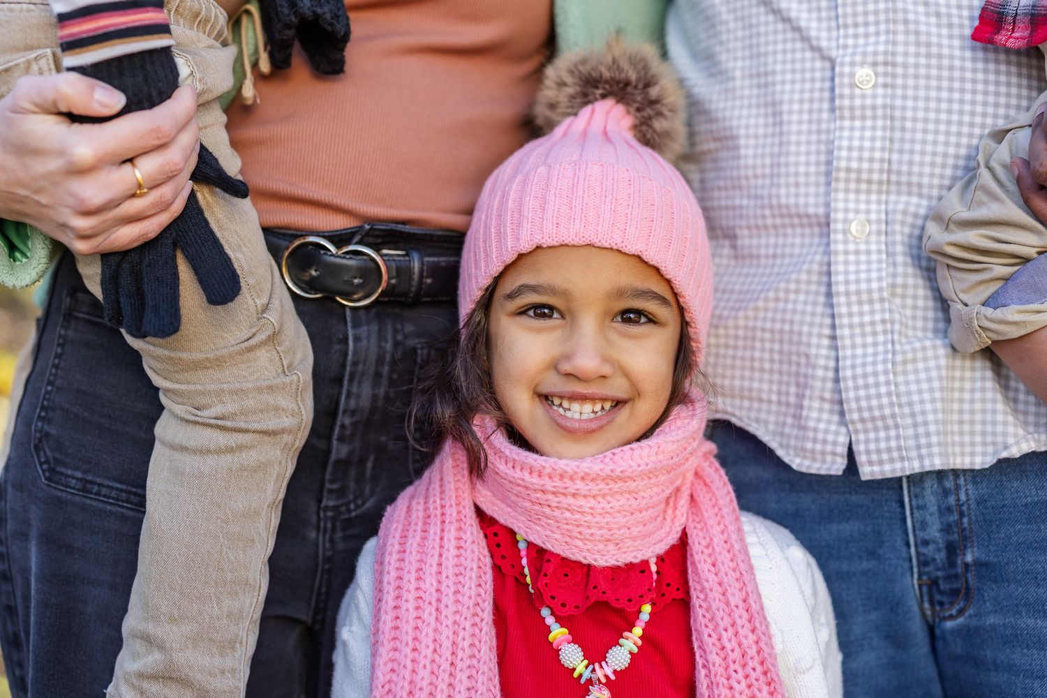 Children wearing colorful winter hats and scarves stand together in a group photo.