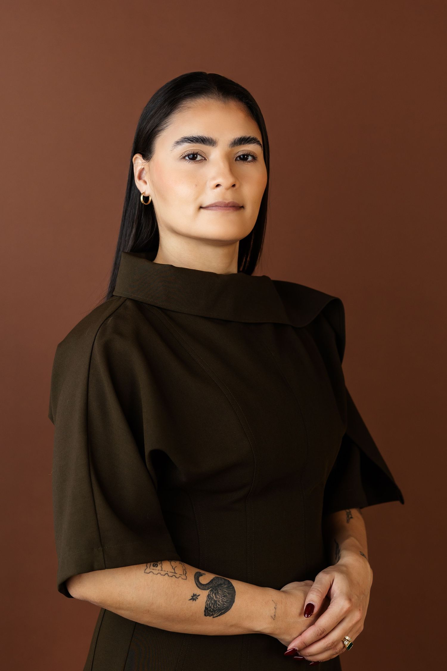Model in black turtleneck top poses against brown background in artistic portrait series.