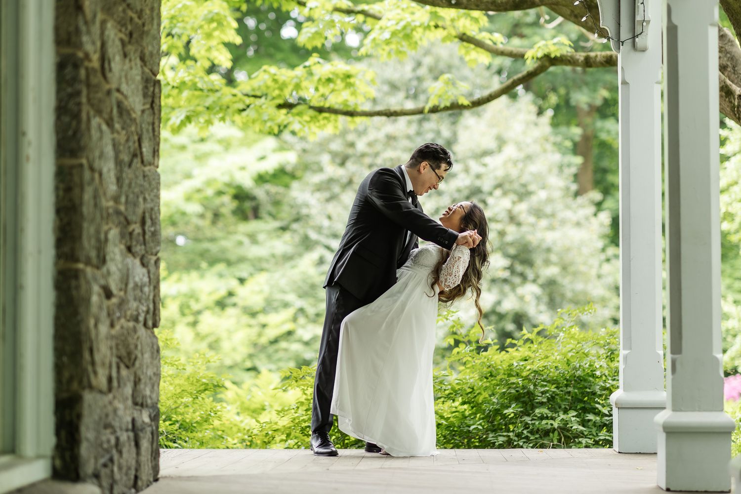A romantic wedding couple embraces under an elegant white gazebo surrounded by lush green foliage.