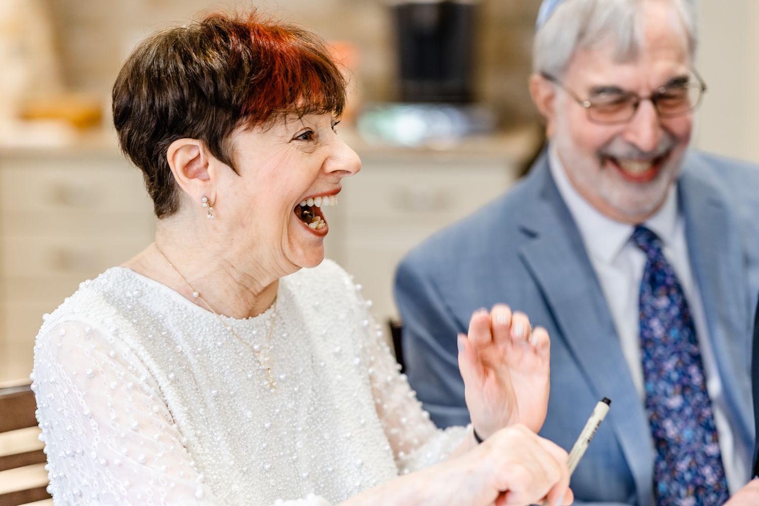 A group of people sitting at a table share joyful laughter during what appears to be a social gathering.