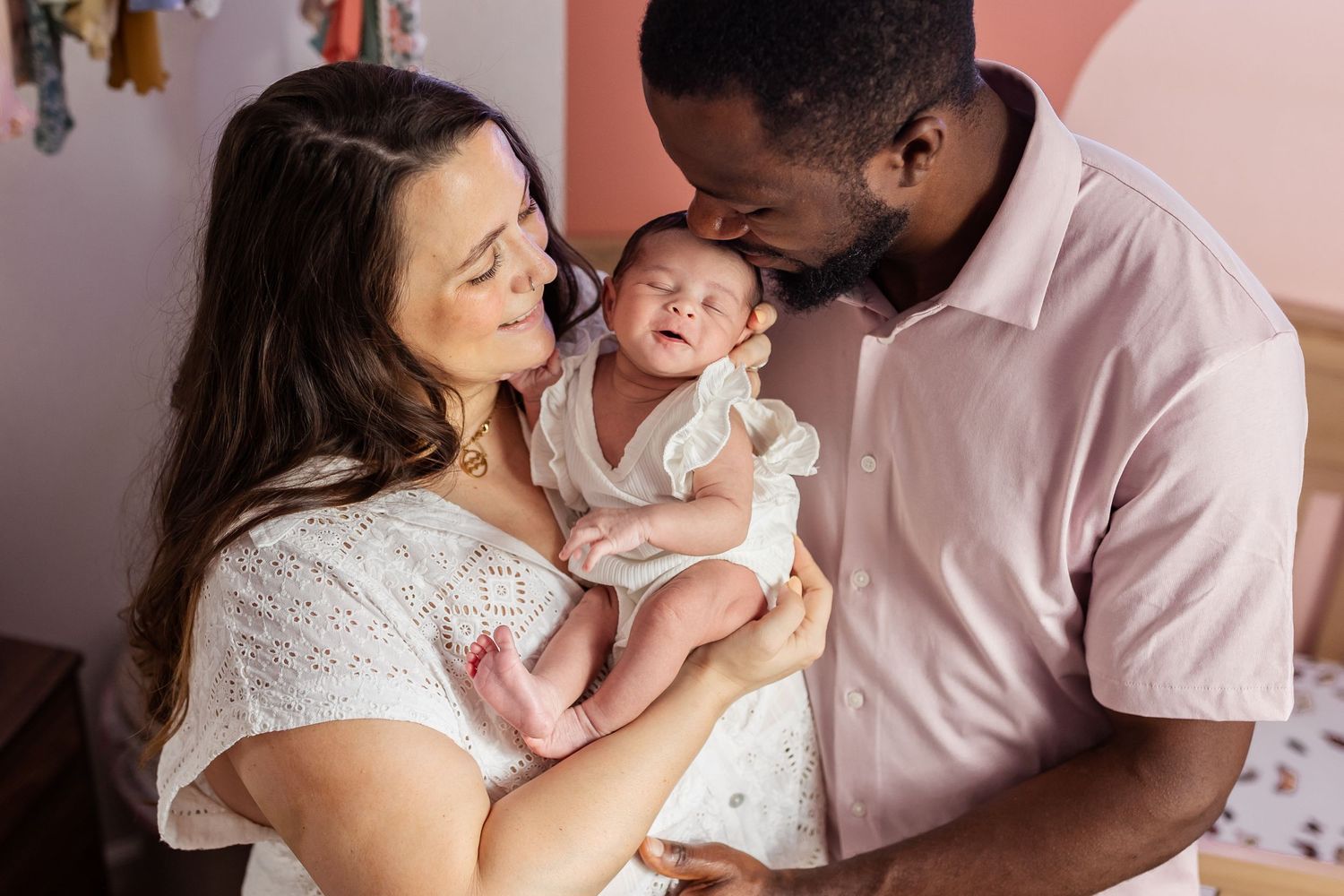 Intimate newborn photography session against a soft pink background capturing tender family moments.