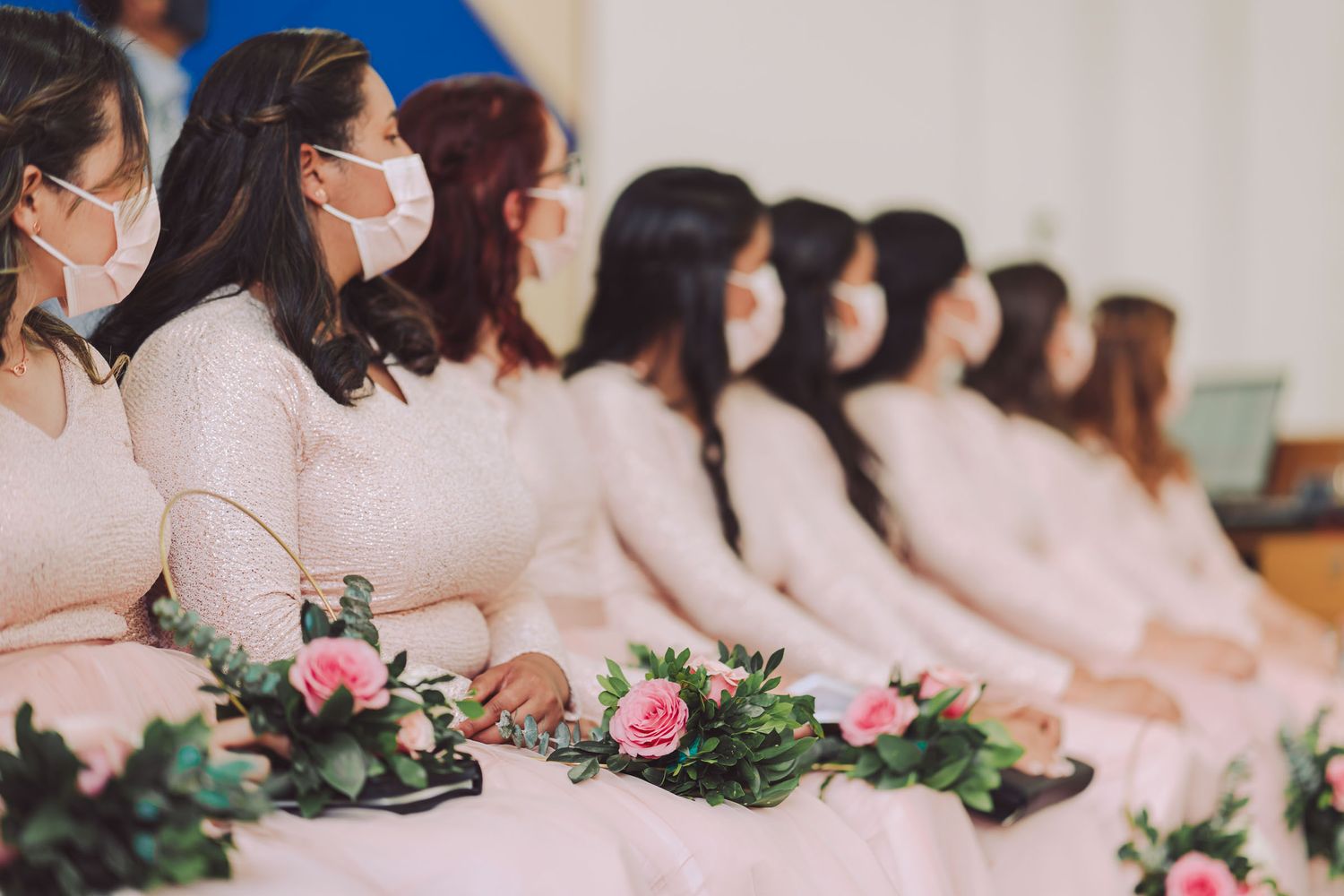 Damas de honor sentadas con vestidos rosados y mascarillas durante la ceremonia.