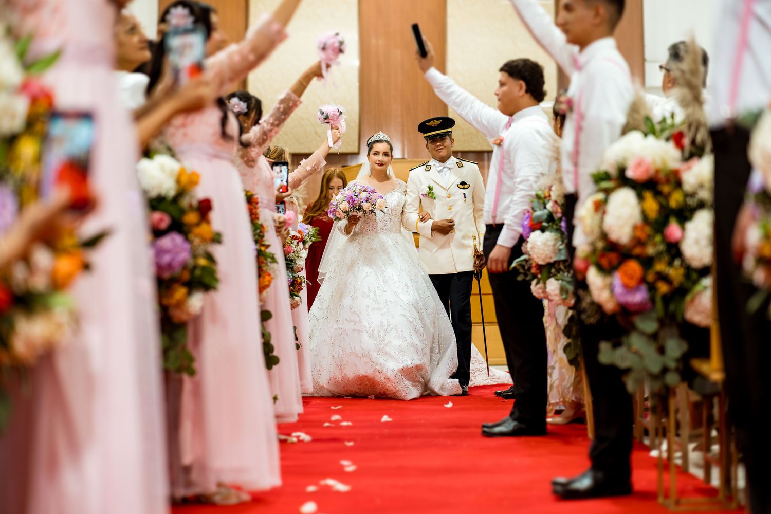 Salida triunfal de los novios de la ceremonia mientras la corte hace arco con ramos de flores y biblias