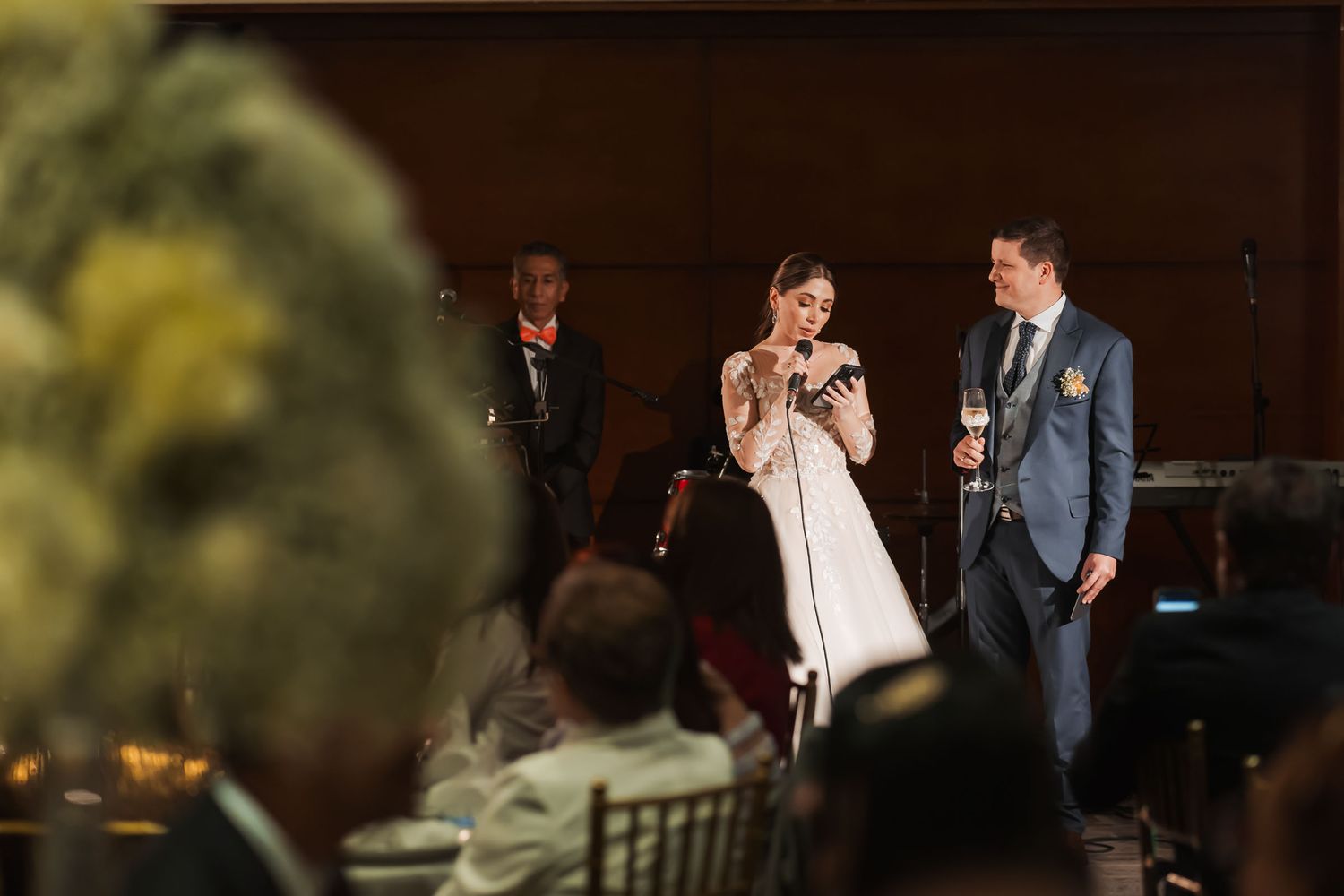 Recién casados dan discurso de agradecimiento en su recepción de boda. Novia habla al micrófono, novio al lado.