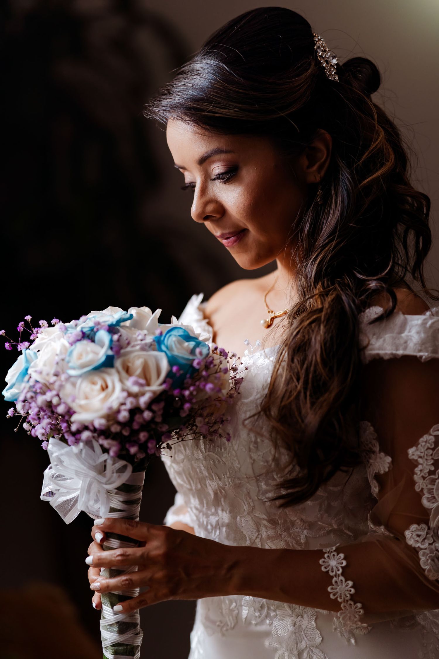 Primer plano de novia mirando su ramo floral con luz dramática. Viste vestido de encaje. Foto de boda emotiva.