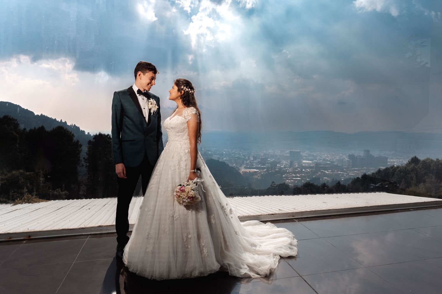 Novios mirándose en balcón con paisaje y rayos de sol celestiales