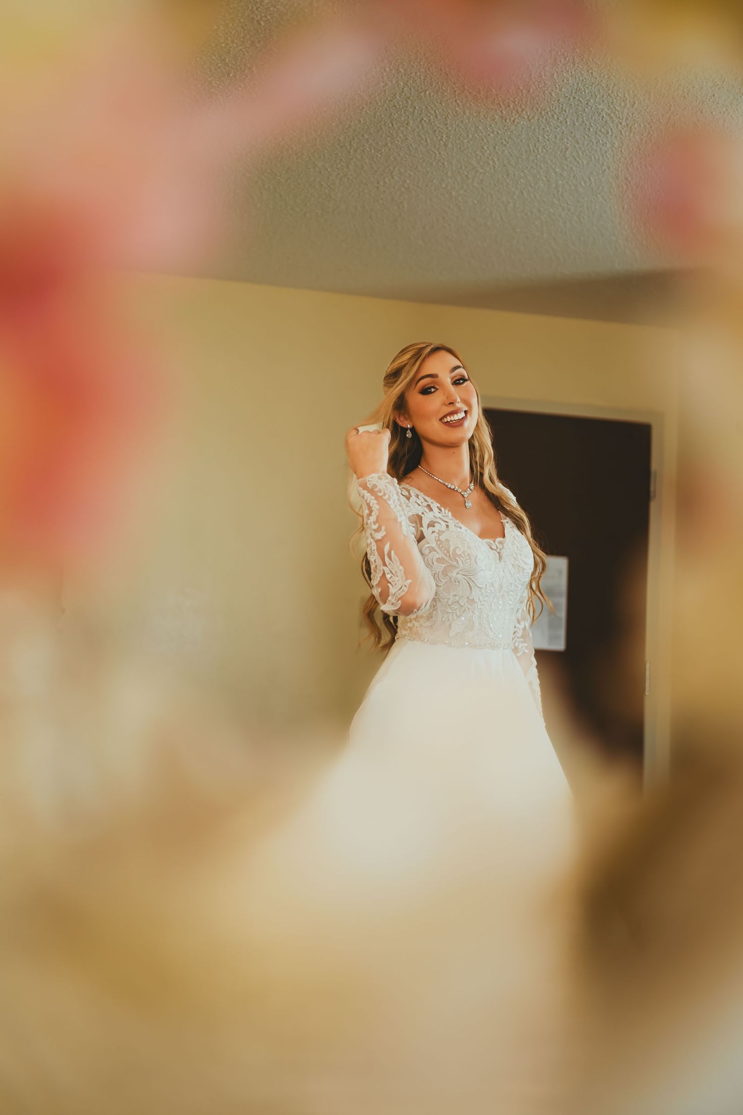 Reflejo de novia sonriente con vestido de encaje y peinado elegante en espejo; preparación boda.