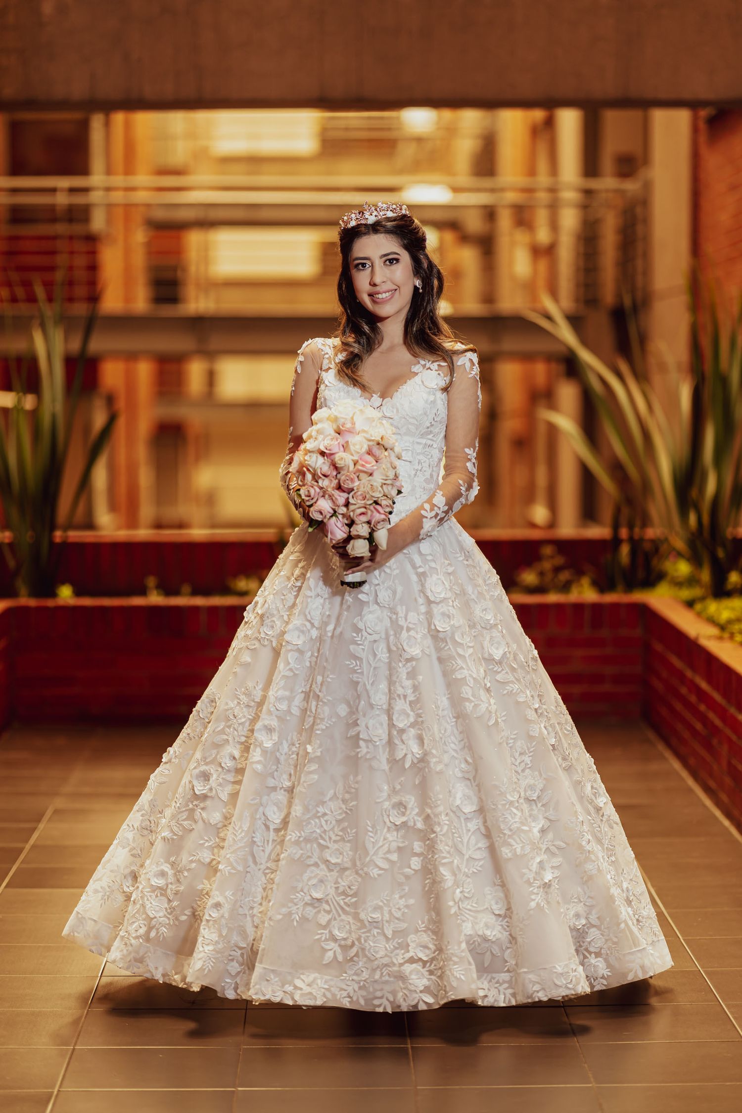 Novia sonriente con vestido princesa y ramo posa en interior moderno con luces cálidas. Fotografía boda.