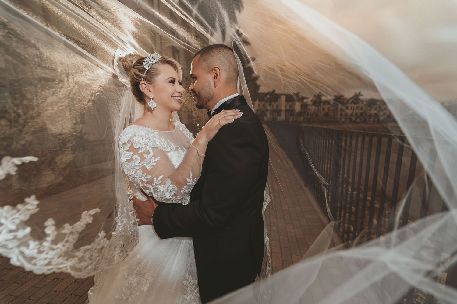 Novios se abrazan y miran bajo el velo transparente de la novia; retrato romántico boda en exterior frente al mar de Miami.