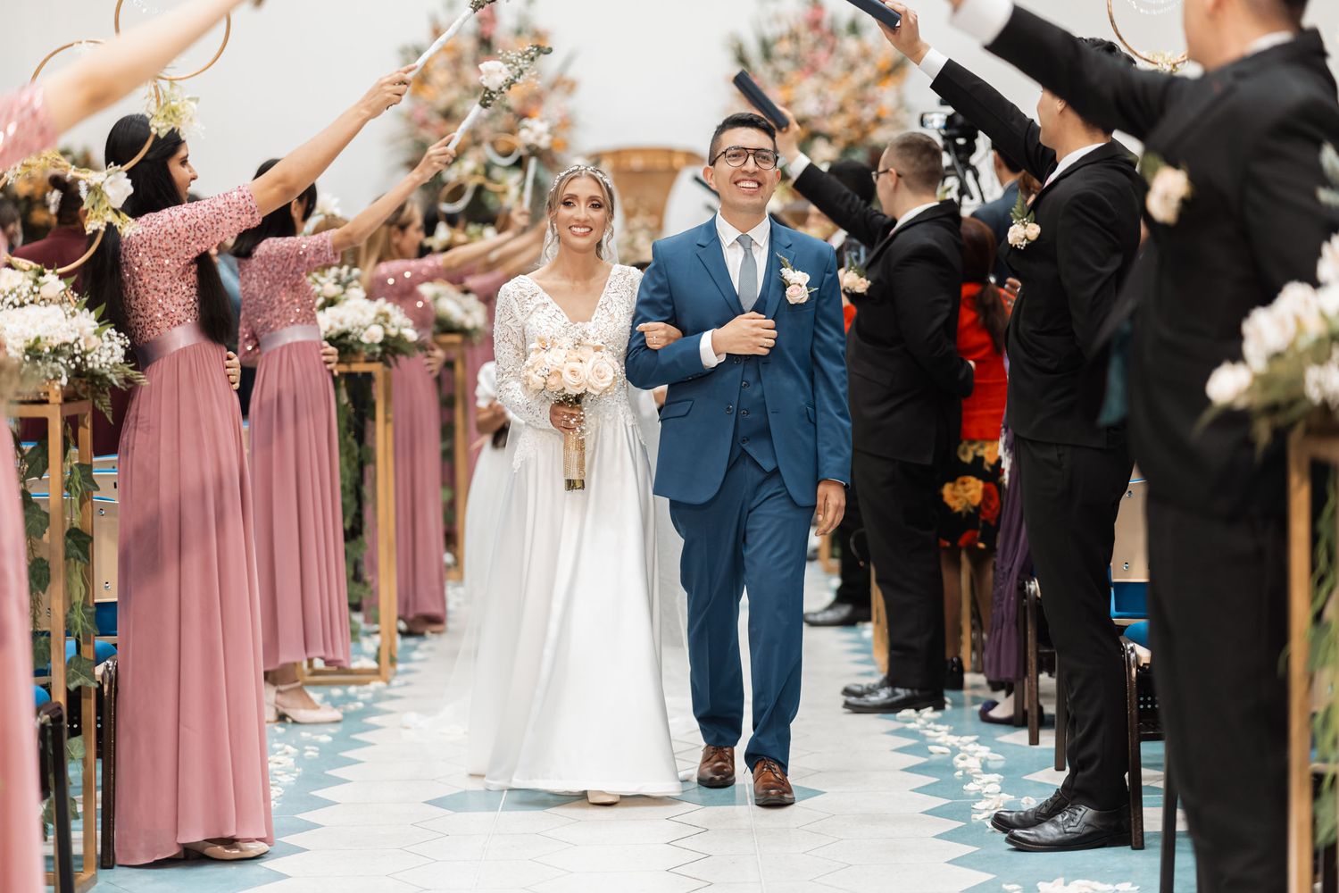 Celebración de boda IDMJI: Novios avanzan por pasillo mientras invitados les reciben con un túnel de rosas y biblias.