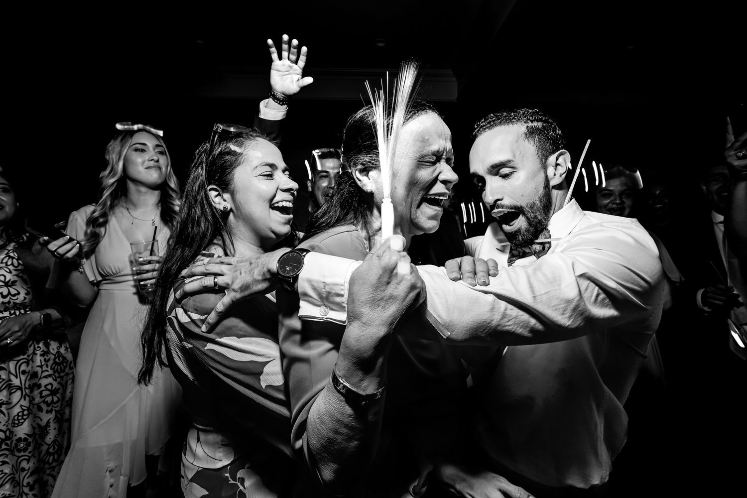 Momento divertido en la pista de baile: Amigos ríen y bailan en fiesta de boda con bengalas. Foto blanco y negro.