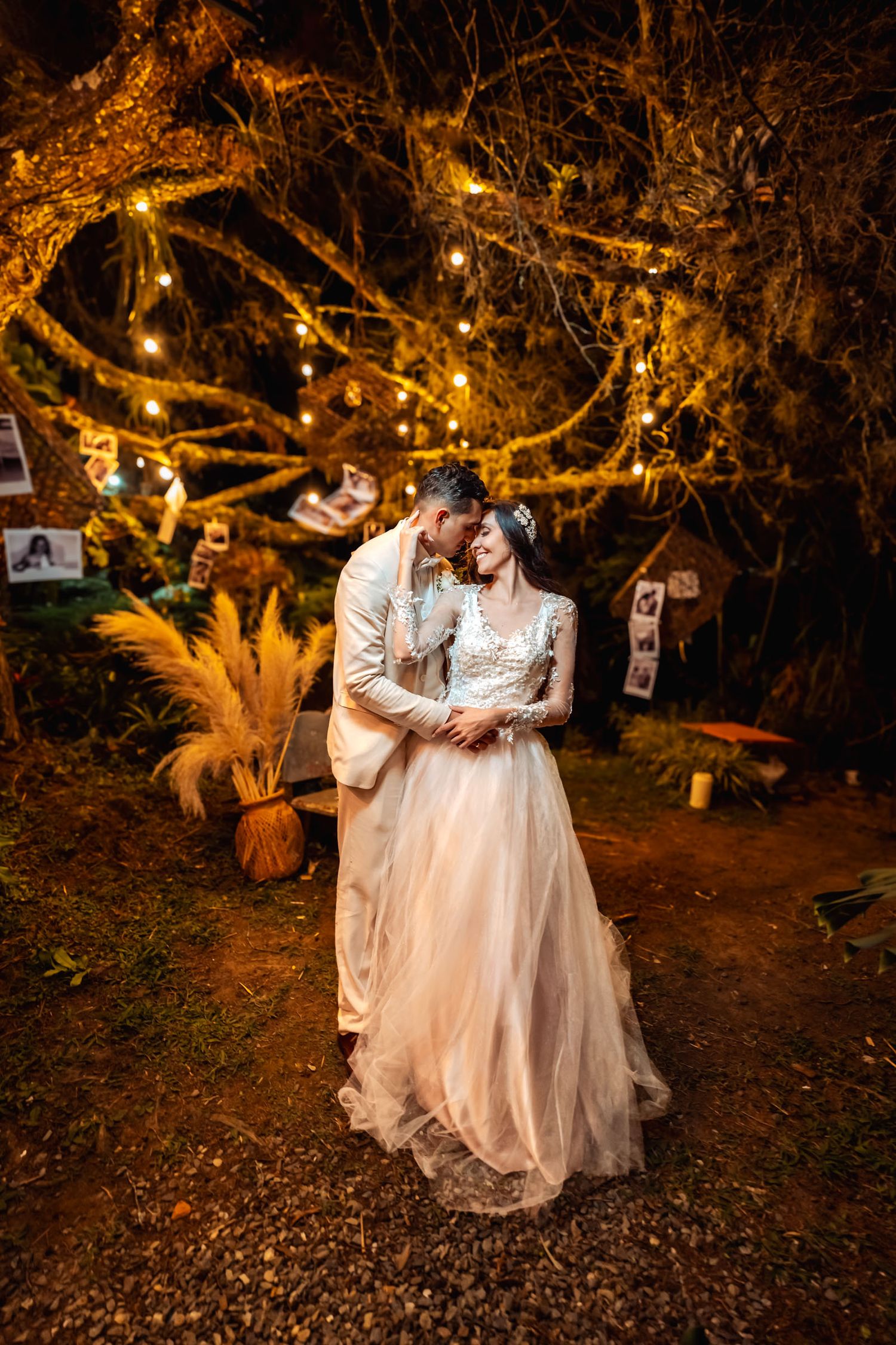 Boda íntima nocturna: novios abrazados bajo árbol con luces cálidas, decoración bohemia. Ambiente romántico y acogedor