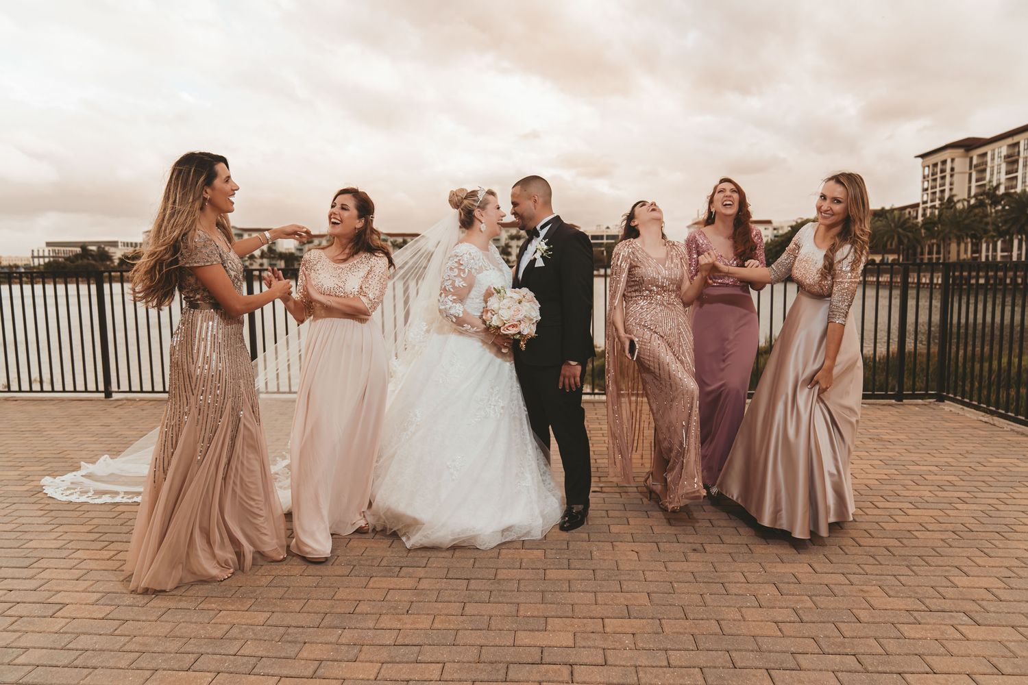 Novios casi besándose rodeados de damas de honor riendo en exterior en un atardecer de Miami; foto divertida boda.